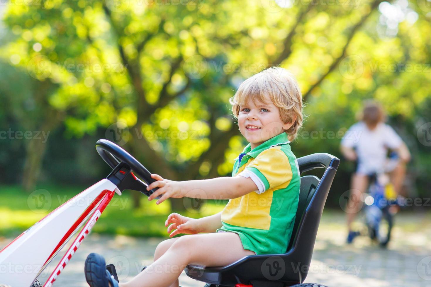 ragazzino attivo alla guida di auto a pedali nel giardino estivo foto
