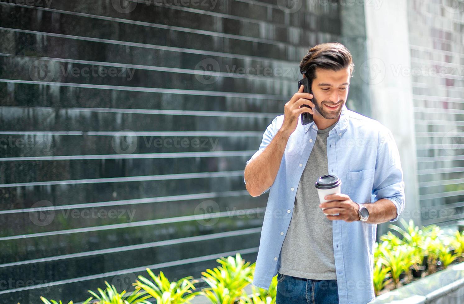 giovane caucasico uomo potabile caffè e utilizzando smartphone parlando con il suo amico mentre a piedi su il suo modo. foto