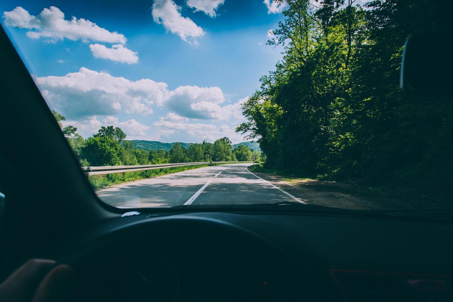 strada, alberi e cielo blu nuvoloso visti attraverso il parabrezza dell'auto foto