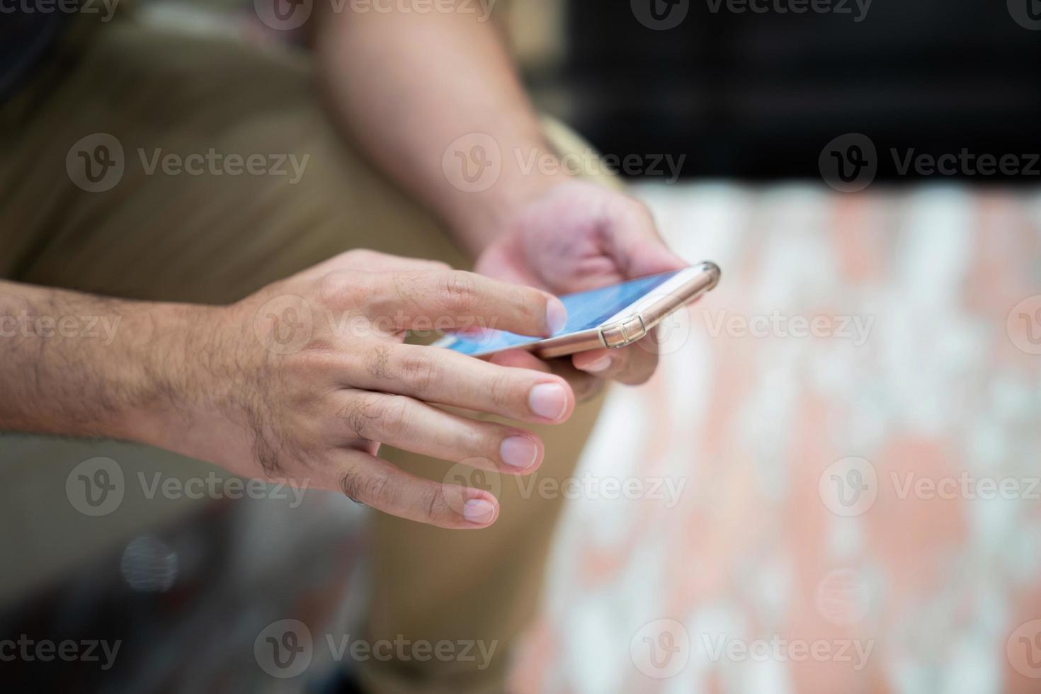 asiatico uomo si siede su il piccolo divano sedia e lavori con il suo mobile Telefono, vuoto chiaro bianca leggero su mobile schermo. foto