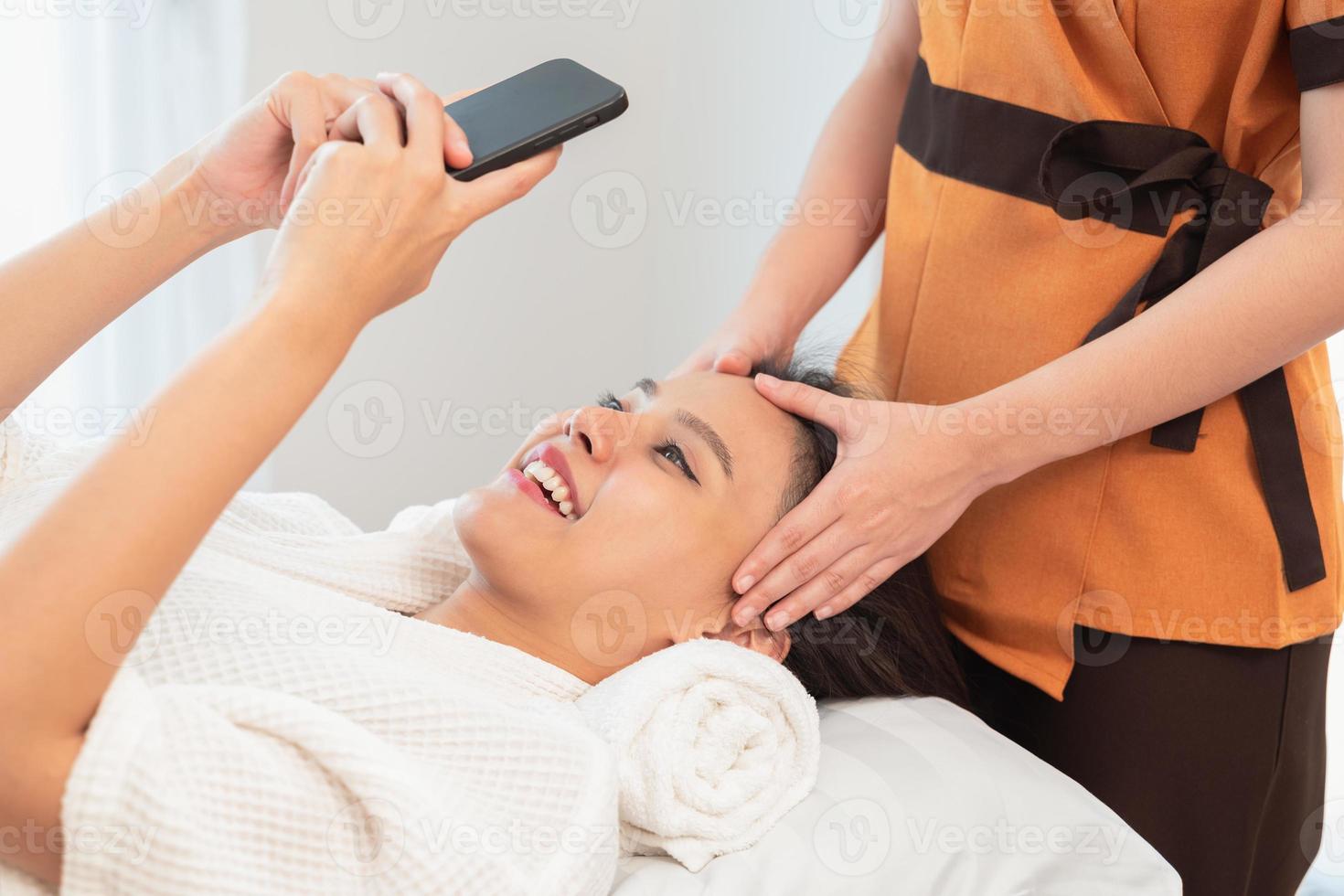 contento giovane donna utilizzando smartphone mentre dire bugie su massaggio tavolo foto