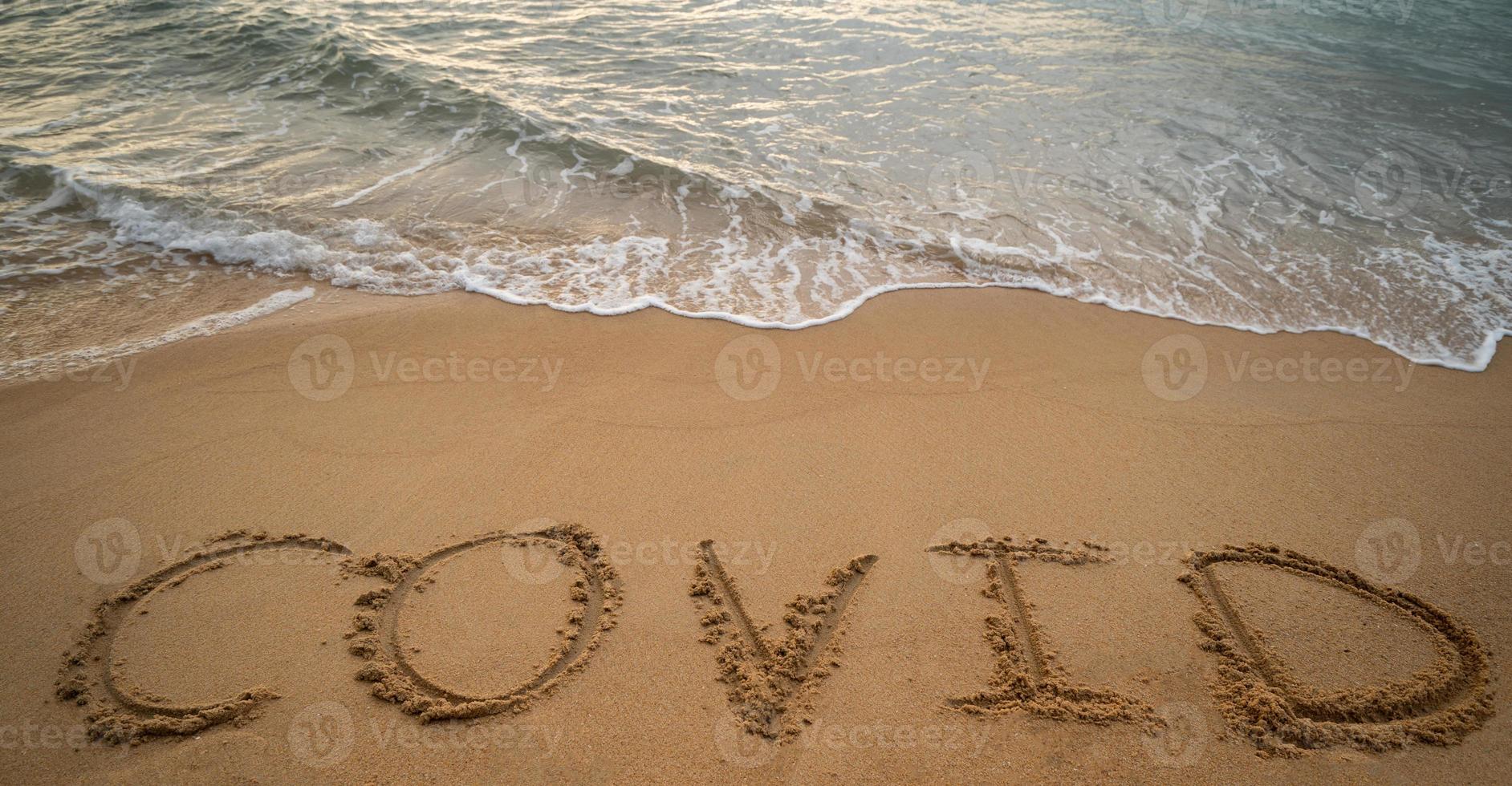 grafia covid su sabbia e schiuma onda su spiaggia. coronavirus concetto. foto