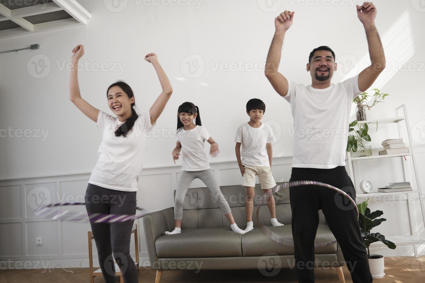 contento benessere asiatico tailandese famiglia, genitori, e bambini siamo divertimento giocando hula cerchi insieme, fitness formazione e salutare esercizio nel bianca vivente camera, domestico casa stile di vita, e fine settimana attività. foto