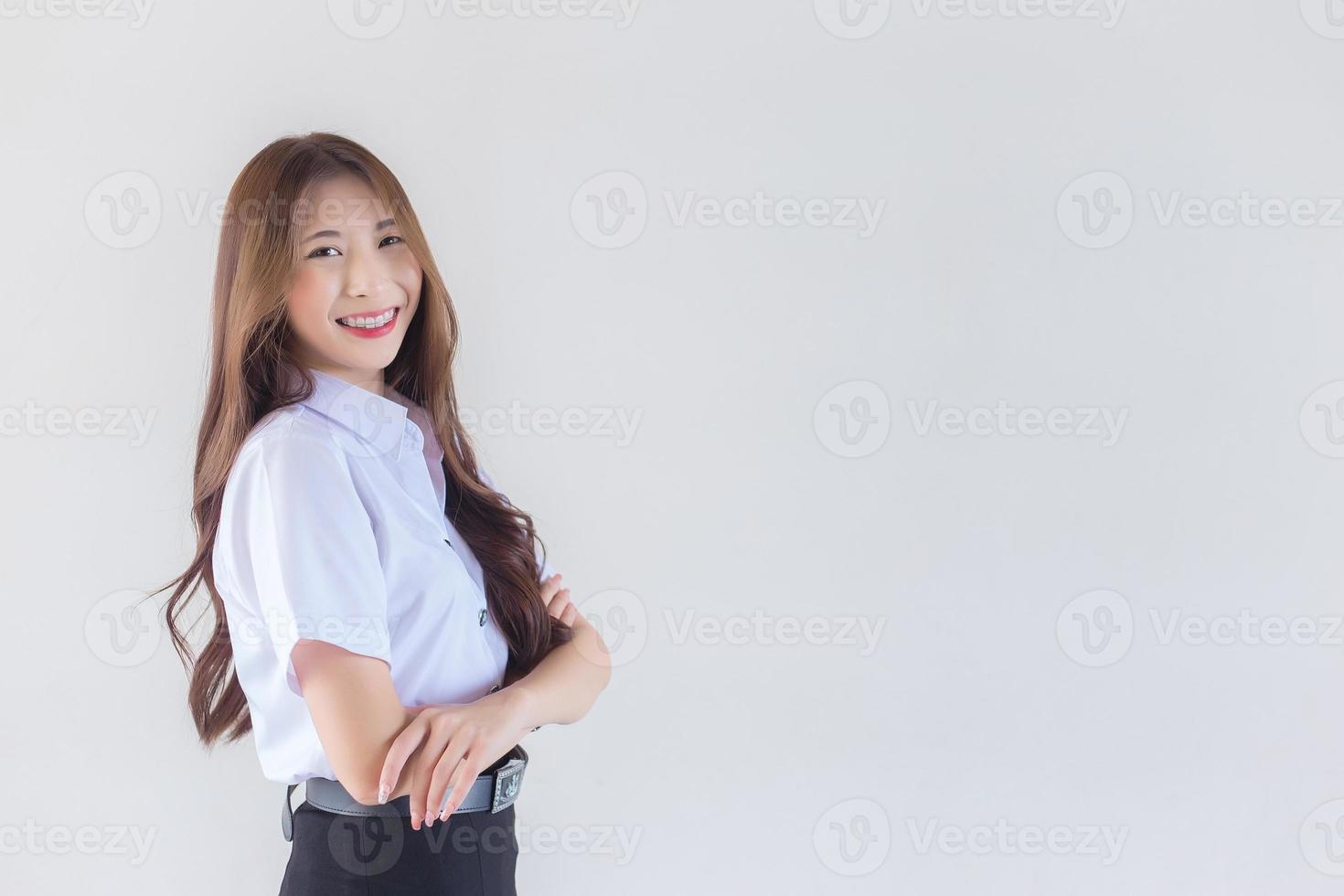 ritratto di un adulto tailandese alunno nel Università alunno uniforme. asiatico bellissimo ragazza in piedi con sua braccia attraversato con fiducia su bianca sfondo. foto