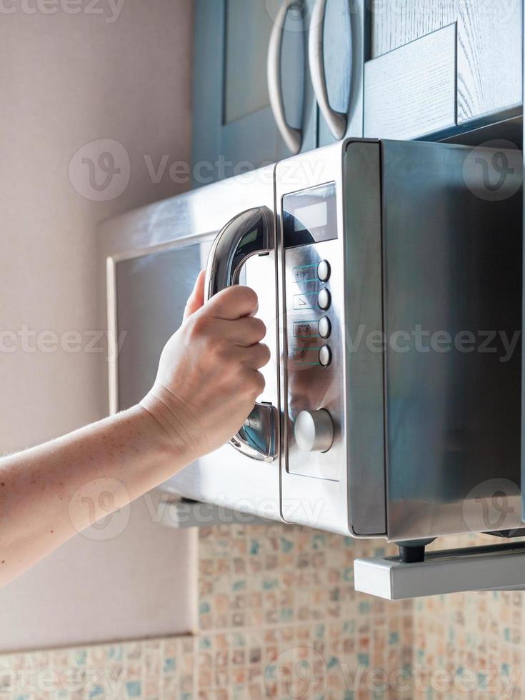 mano si chiude microonde forno per riscaldamento cibo foto