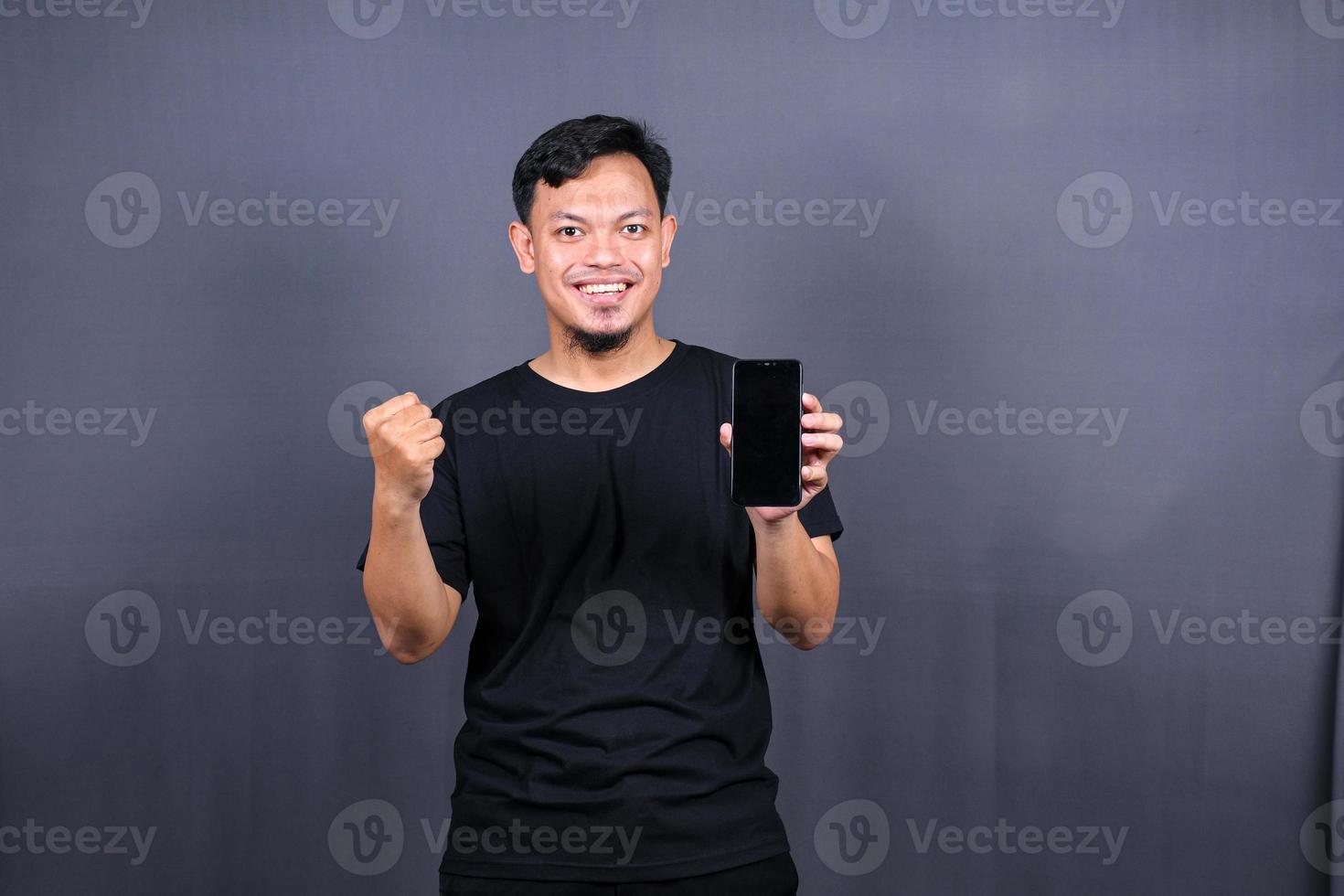 contento asiatico uomo Tenere un' smartphone e vincente il premio. isolato su grigio sfondo foto