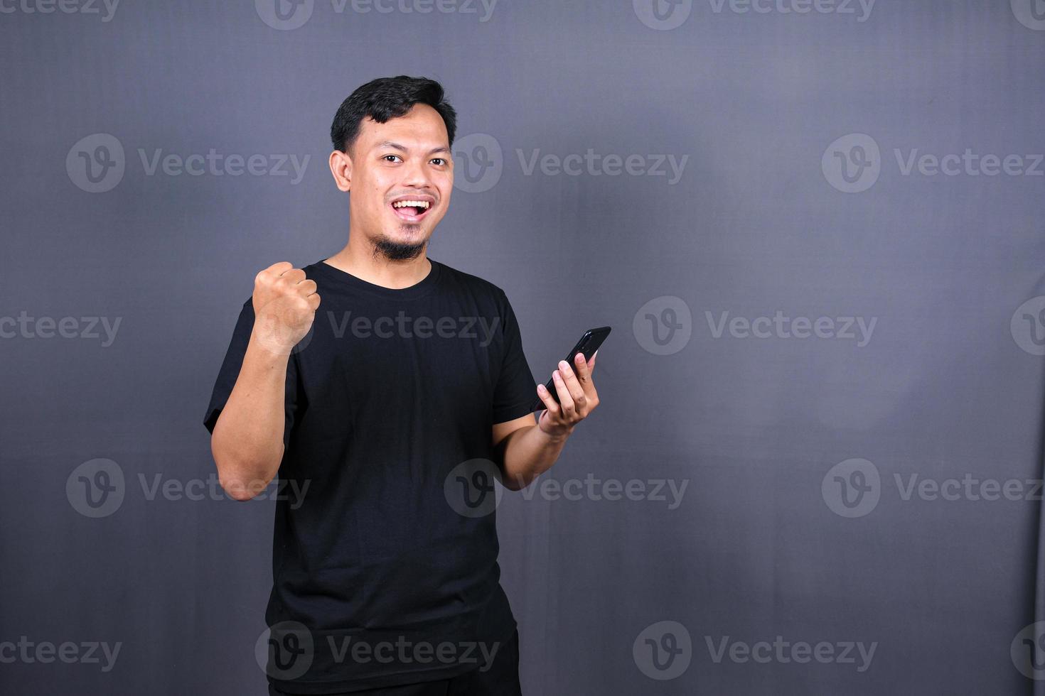 contento asiatico uomo Tenere un' smartphone e vincente il premio. isolato su grigio sfondo foto