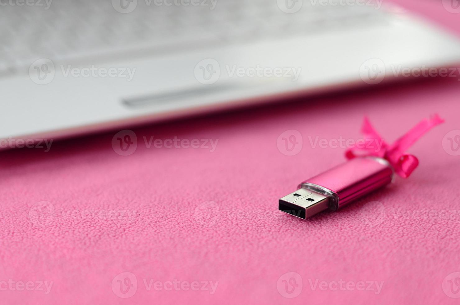 brillante rosa USB veloce memoria carta con un' rosa arco bugie su un' coperta di morbido e peloso leggero rosa vello tessuto accanto per un' bianca il computer portatile. classico femmina regalo design per un' memoria carta foto