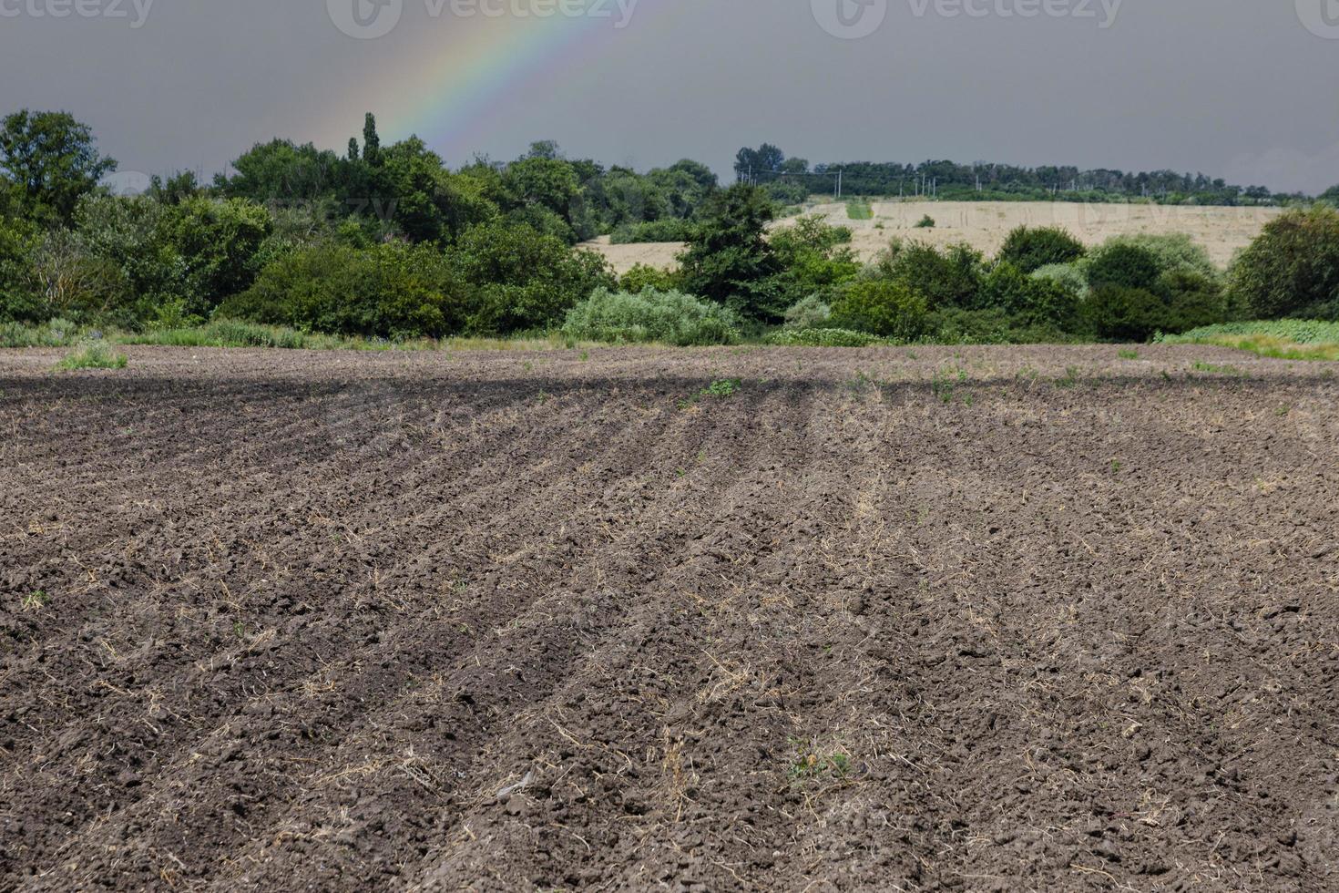 modello di righe nel arabile terra contro il sfondo di un' arcobaleno e un' piovoso cielo. foto