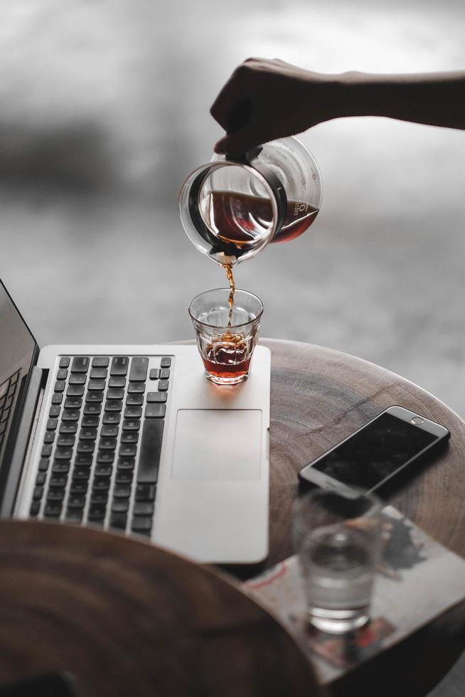 persona che versa il tè nella tazza sul computer portatile foto