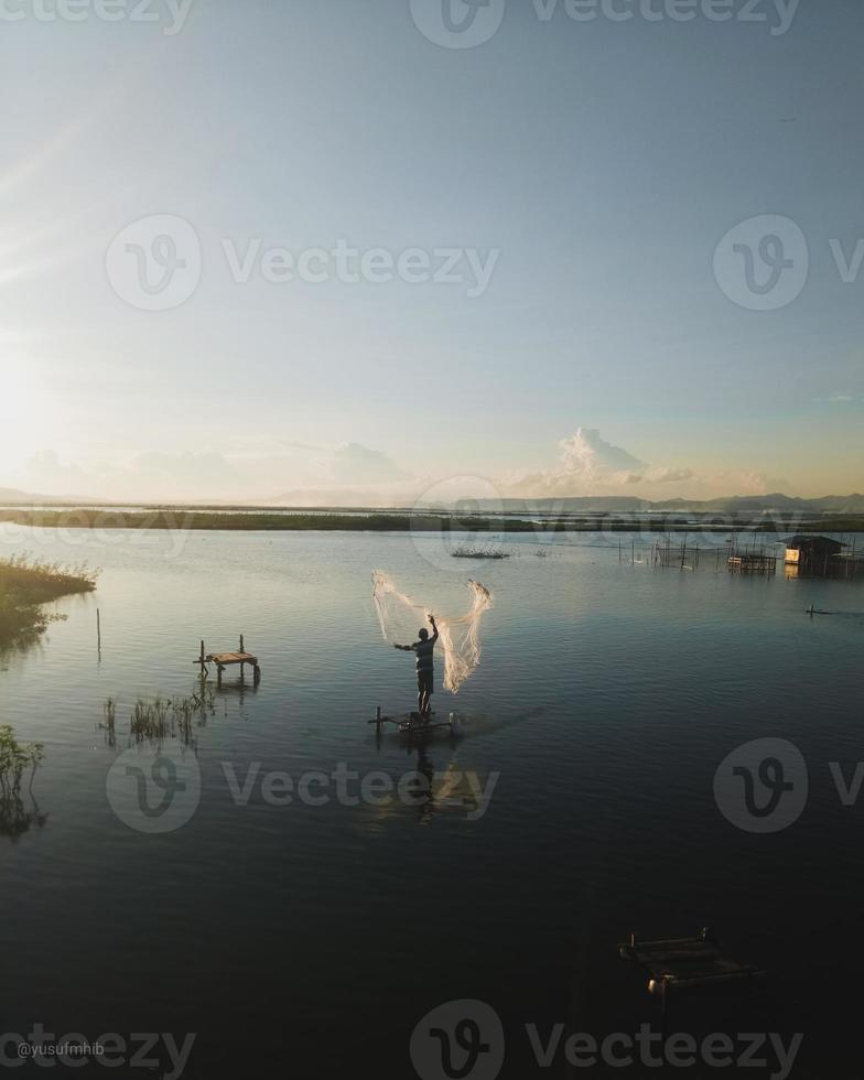 silhouette di un' uomo pesca nel il pomeriggio. tramonto su lago limbo, Indonesia foto