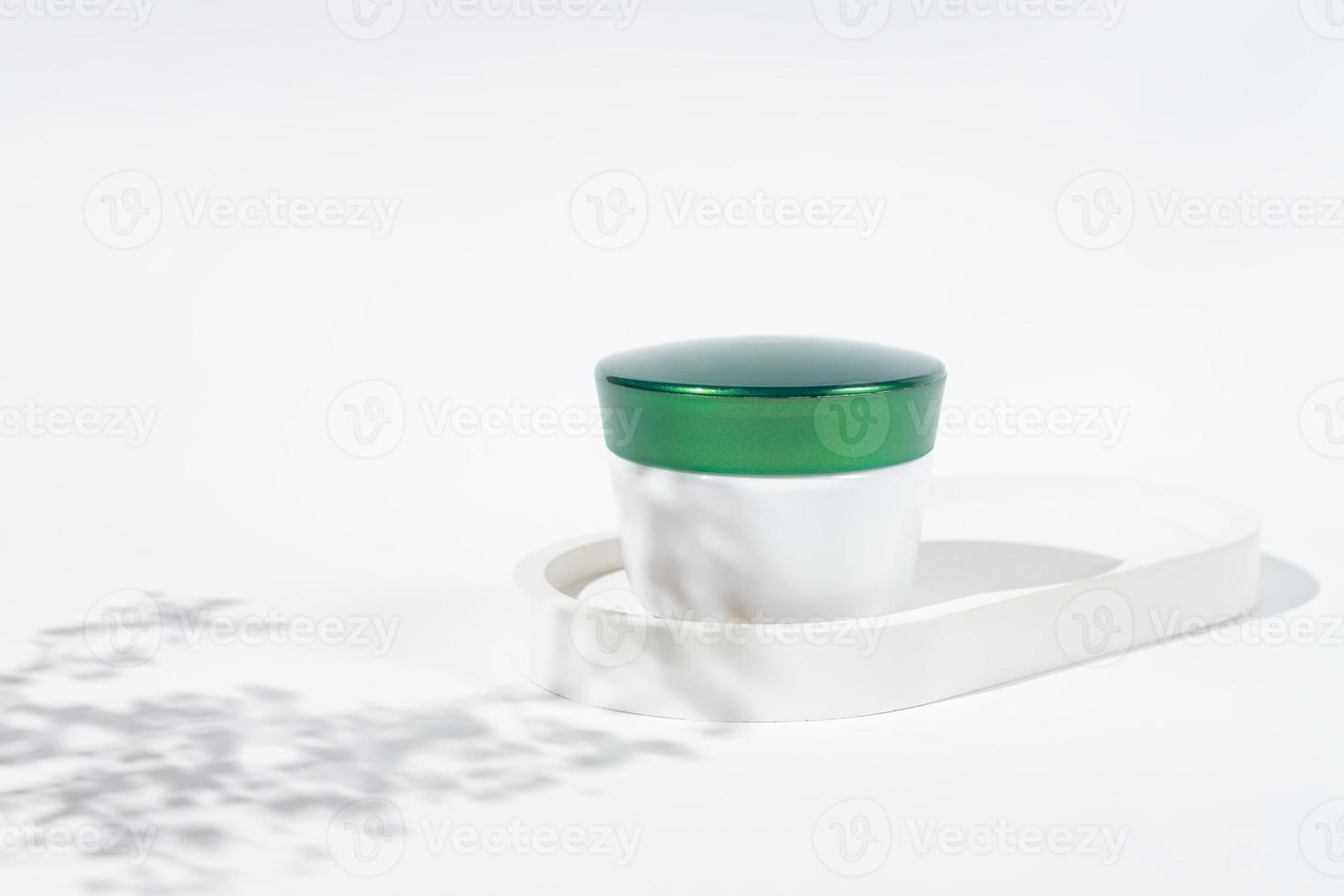 verde coperchio plastica vaso con aspetto di il crema su bianca sfondo con fiori ombra. cura della pelle prodotti , naturale cosmetico. bellezza concetto per viso corpo cura foto