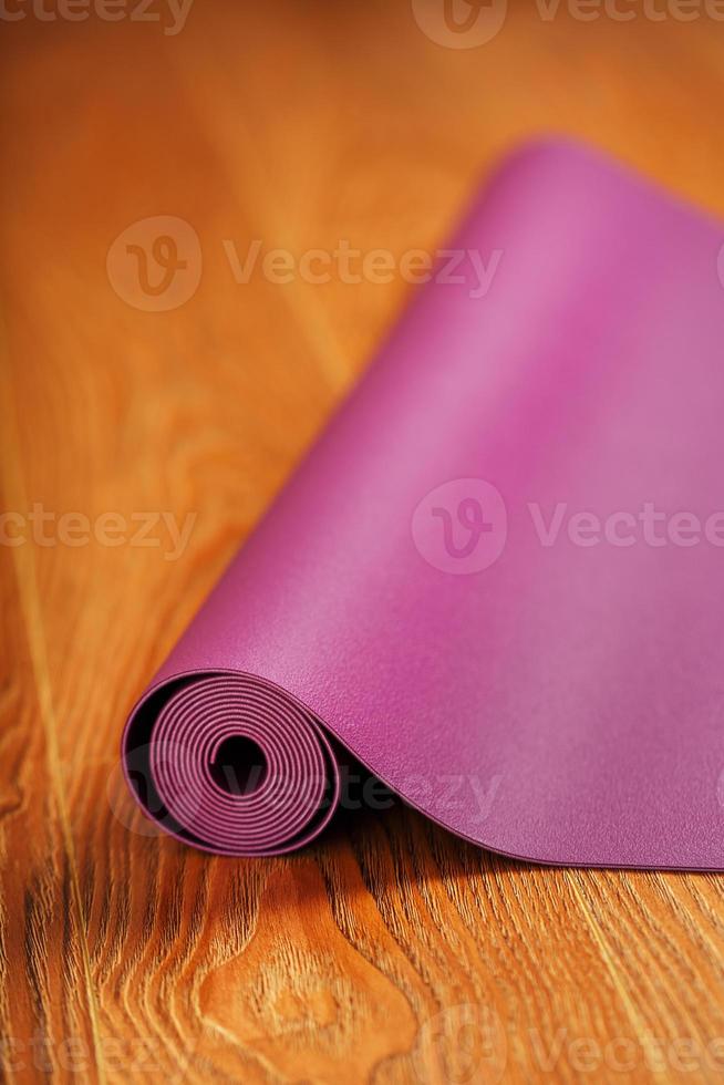 un' lilla yoga stuoia è contorto su il di legno pavimento. foto