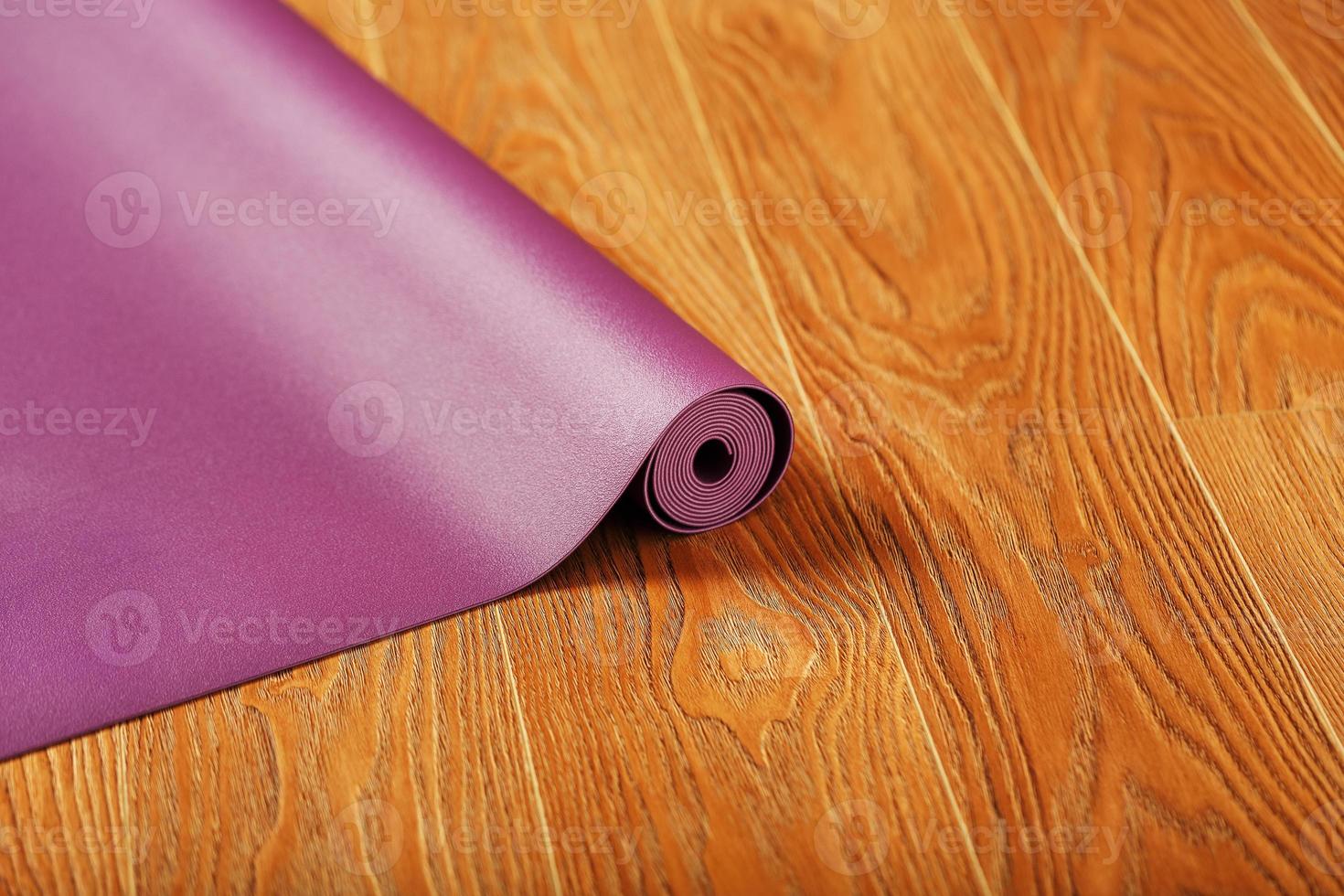un' color lilla yoga stuoia è diffusione su nel un' rotolo su il di legno pavimento. foto