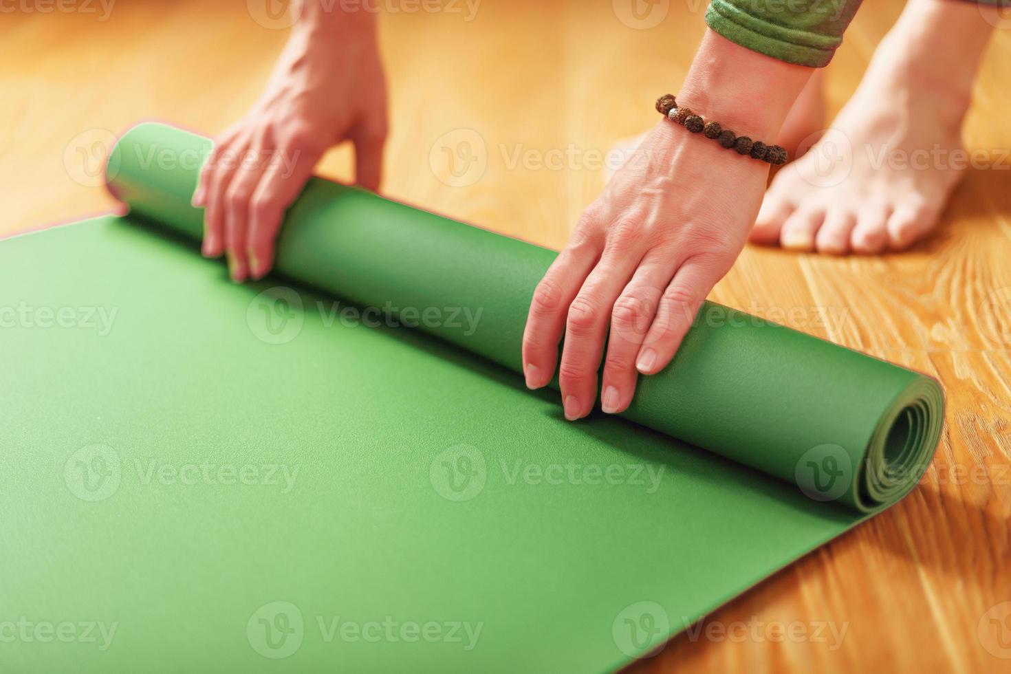 un' donna rotoli su un' verde stuoia prima un' yoga classe foto