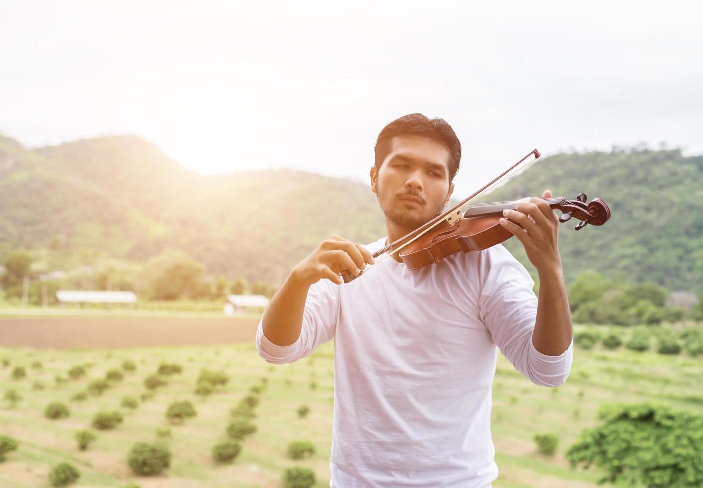 giovane musicista hipster che suona il violino nello stile di vita all'aperto della natura dietro la montagna. foto