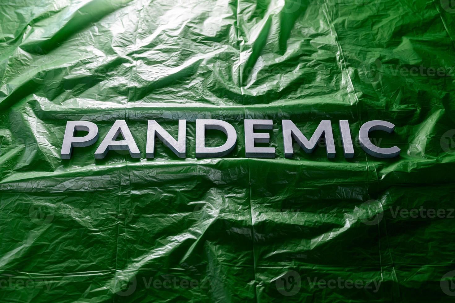 il parola pandemia di cui con argento lettere su spiegazzato verde plastica film sfondo. inclinato prospettiva. foto