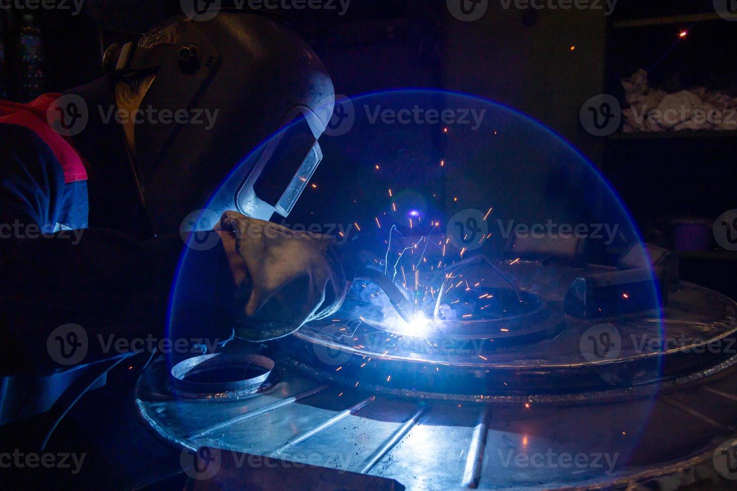 un' lente bagliore mentre Manuale semiautomatico elettrico saldatura con scintille, professionale industriale lavoratore nel nero protettivo maschera. foto