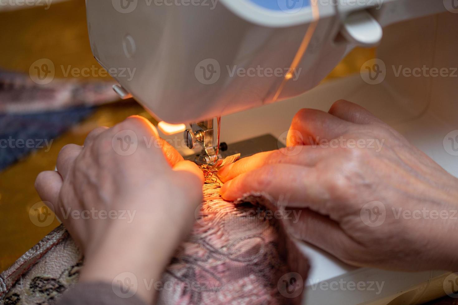 un' avvicinamento Visualizza di cucire processi, mano di vecchio donna utilizzando cucire macchina, selettivo messa a fuoco tecnica foto