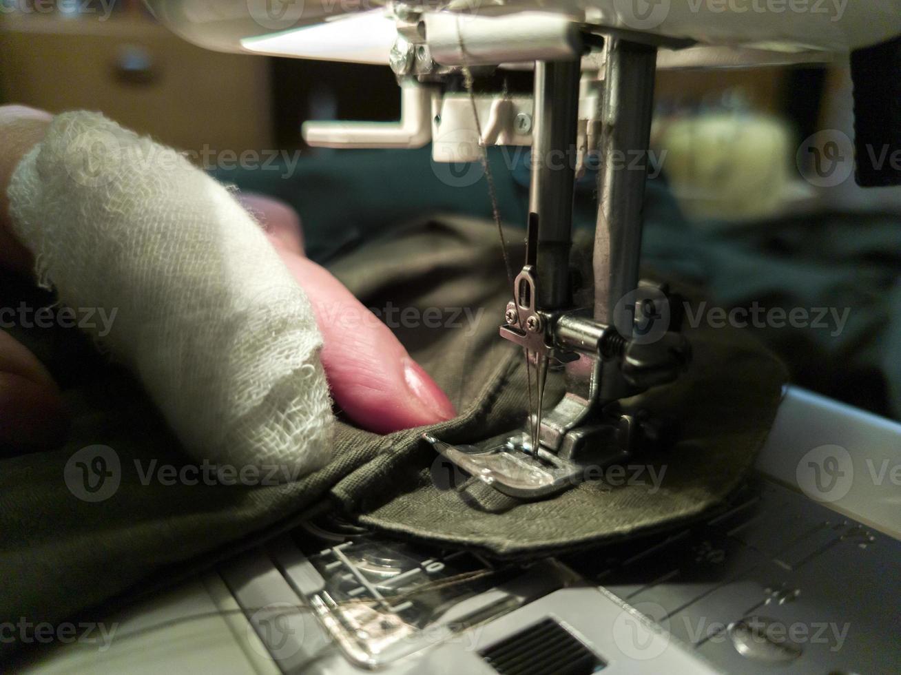 un' mano di anziano womans con un' bendato dito cuce con un' cucire macchina foto