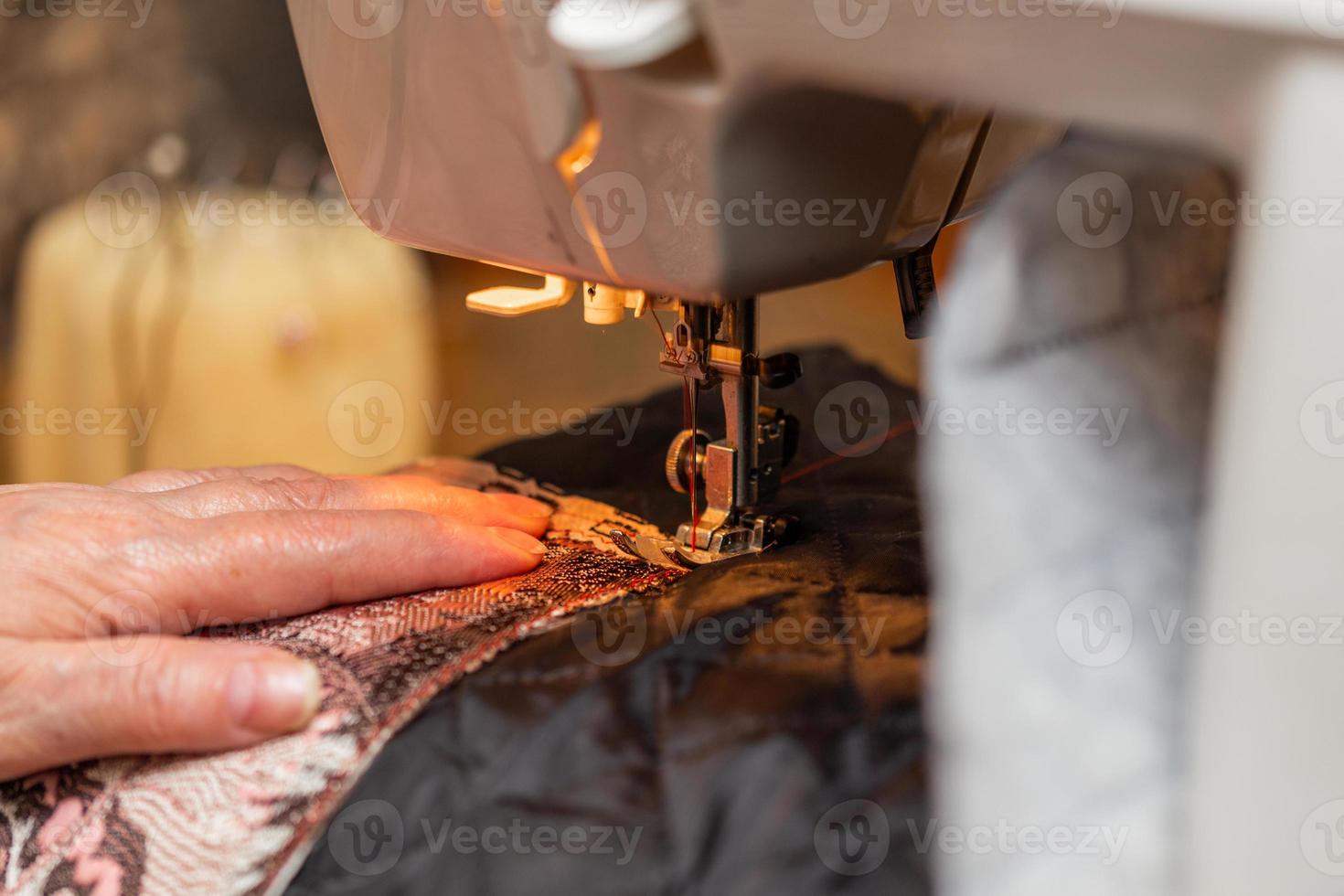 un' avvicinamento Visualizza di cucire processi, mano di vecchio donna utilizzando cucire macchina, selettivo messa a fuoco tecnica foto