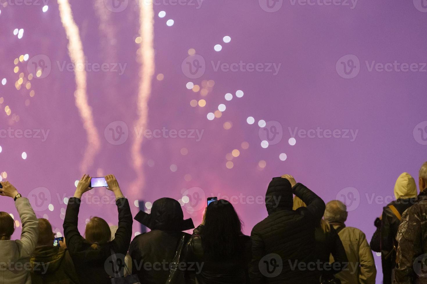 Visualizza a partire dal il indietro a persone nel wark Abiti tiro fuochi d'artificio su il Telefono a freddo notte. foto