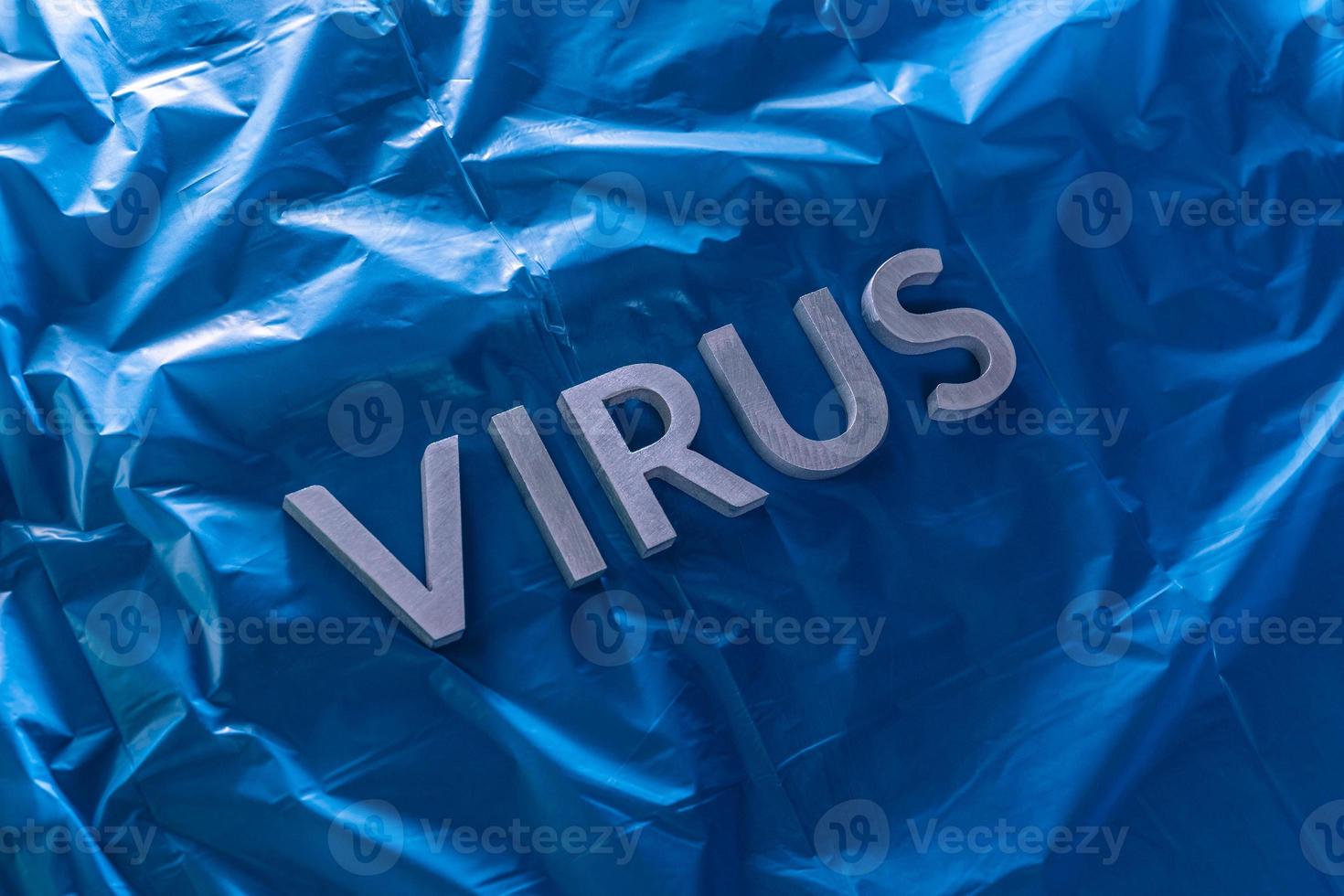 il parola virus di cui con argento metallo lettere su spiegazzato blu plastica film con drammatico leggero foto