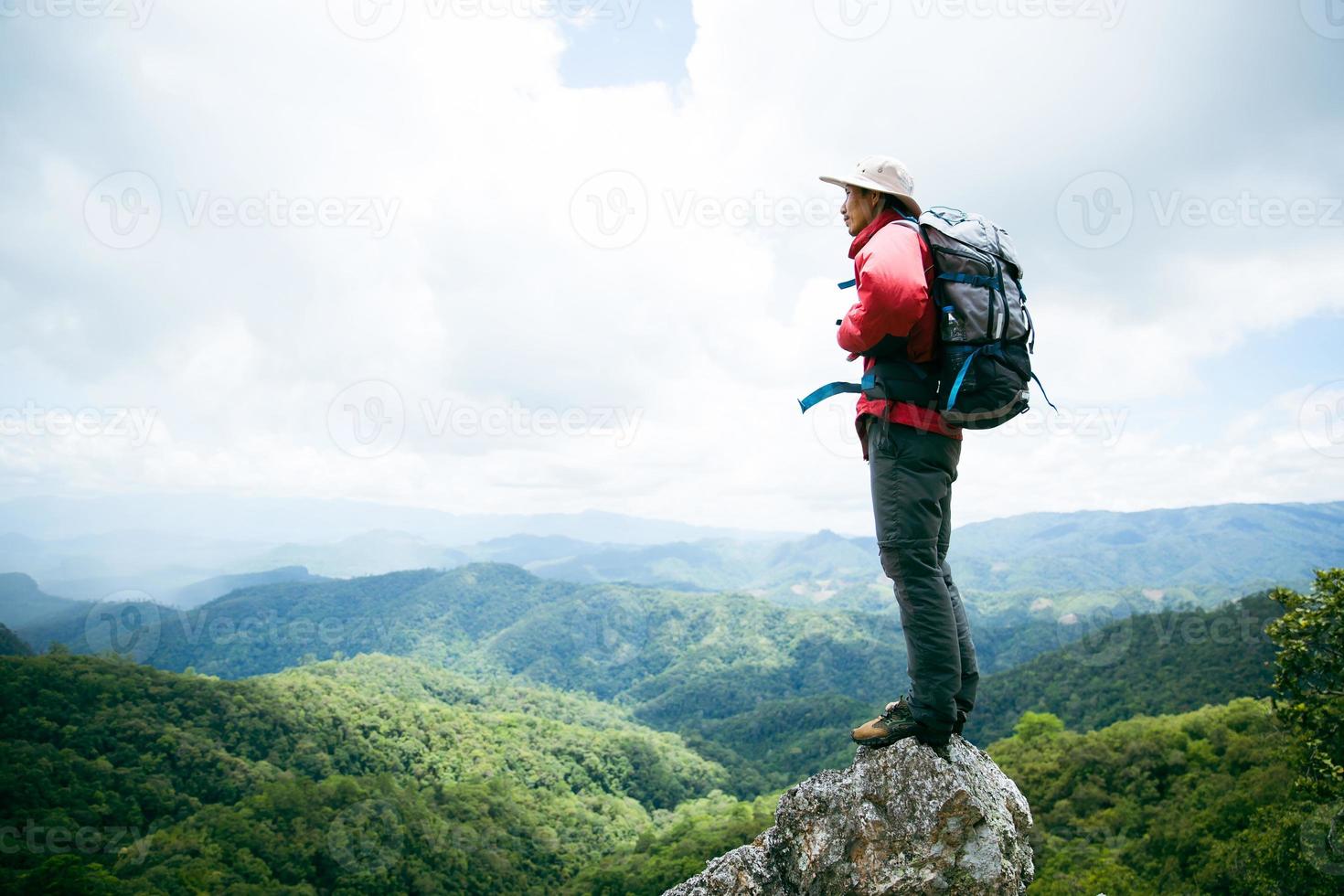 giovane escursionismo maschio sulla roccia in alto, zaino uomo che guarda la bellissima valle di montagna alla luce del sole in estate, paesaggio con uomo sportivo, alte colline, foresta, cielo. viaggi e turismo. foto