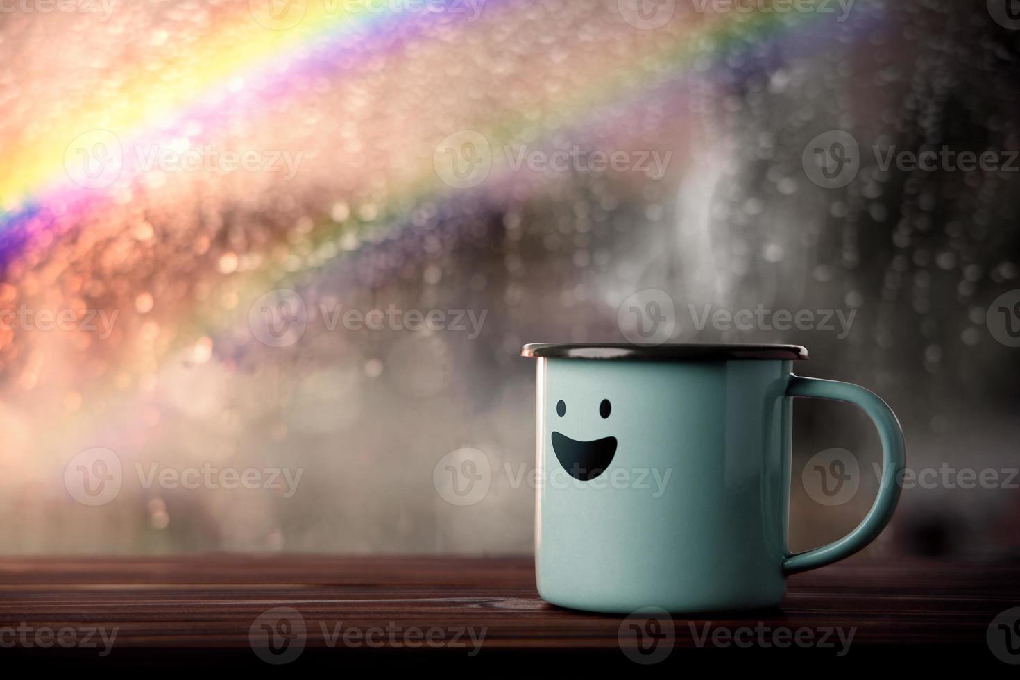 felicità e positivo mente, mentale Salute concetto. godendo caffè con sorridente viso cartone animato, sfocato pioggia con arcobaleno come al di fuori Visualizza. Sorridi su piovoso giorno foto