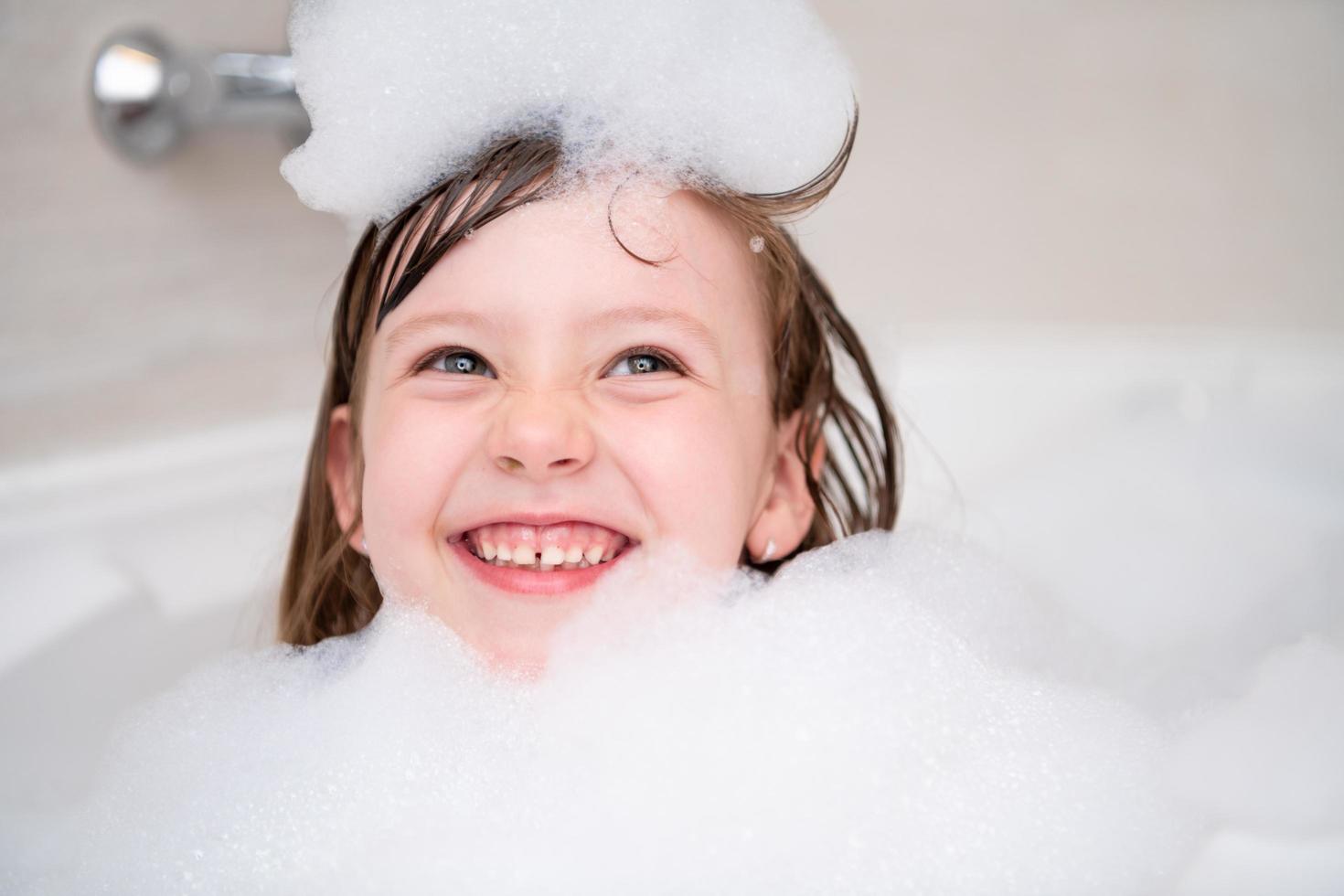 poco ragazza nel bagno giocando con schiuma foto