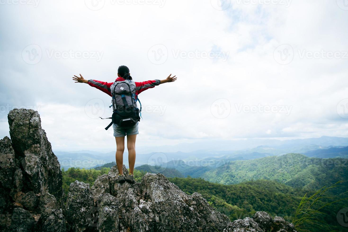 giovane donna escursionismo in piedi sulla roccia in alto, donna zaino che guarda la bellissima valle di montagna alla luce del sole in estate, paesaggio con ragazza sportiva, alte colline, foresta, cielo. viaggi e turismo. foto