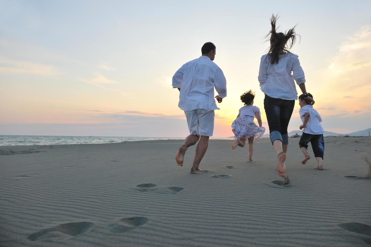 contento giovane famiglia avere divertimento su spiaggia a tramonto foto