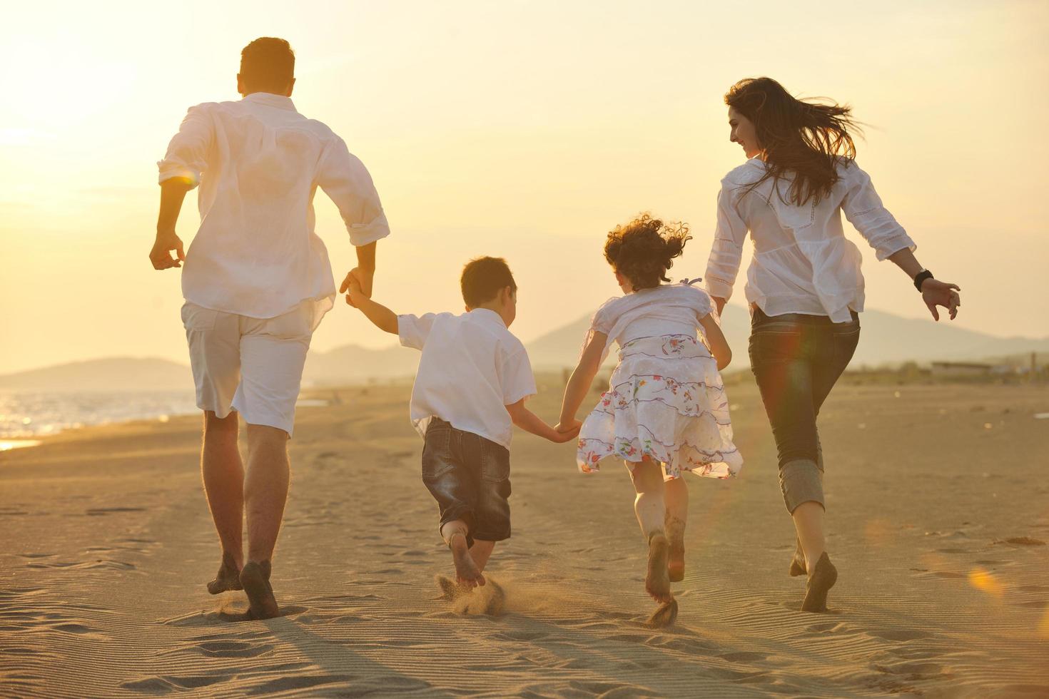 contento giovane famiglia avere divertimento su spiaggia a tramonto foto