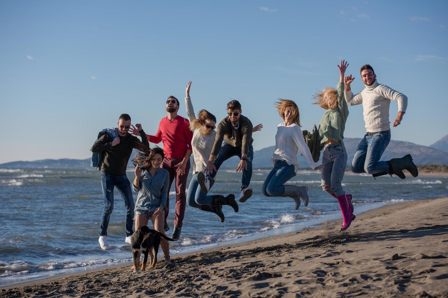 giovane amici salto insieme a autunno spiaggia foto