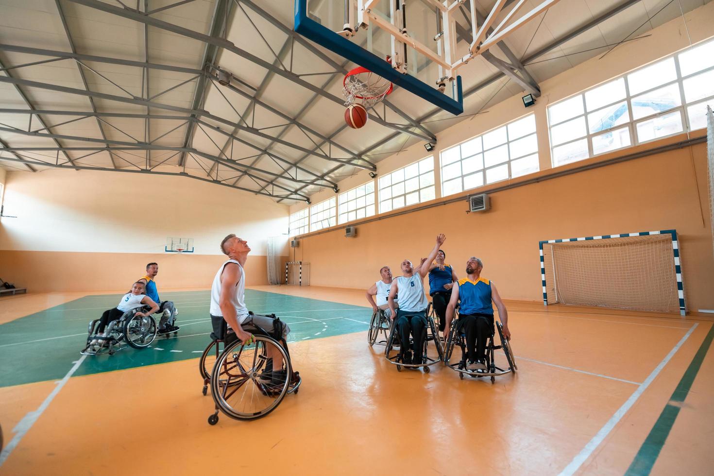 Disabilitato guerra veterani misto gara e età pallacanestro squadre nel sedie a rotelle giocando un' formazione incontro nel un' gli sport Palestra sala. portatori di handicap persone reinserimento e inclusione concetto foto