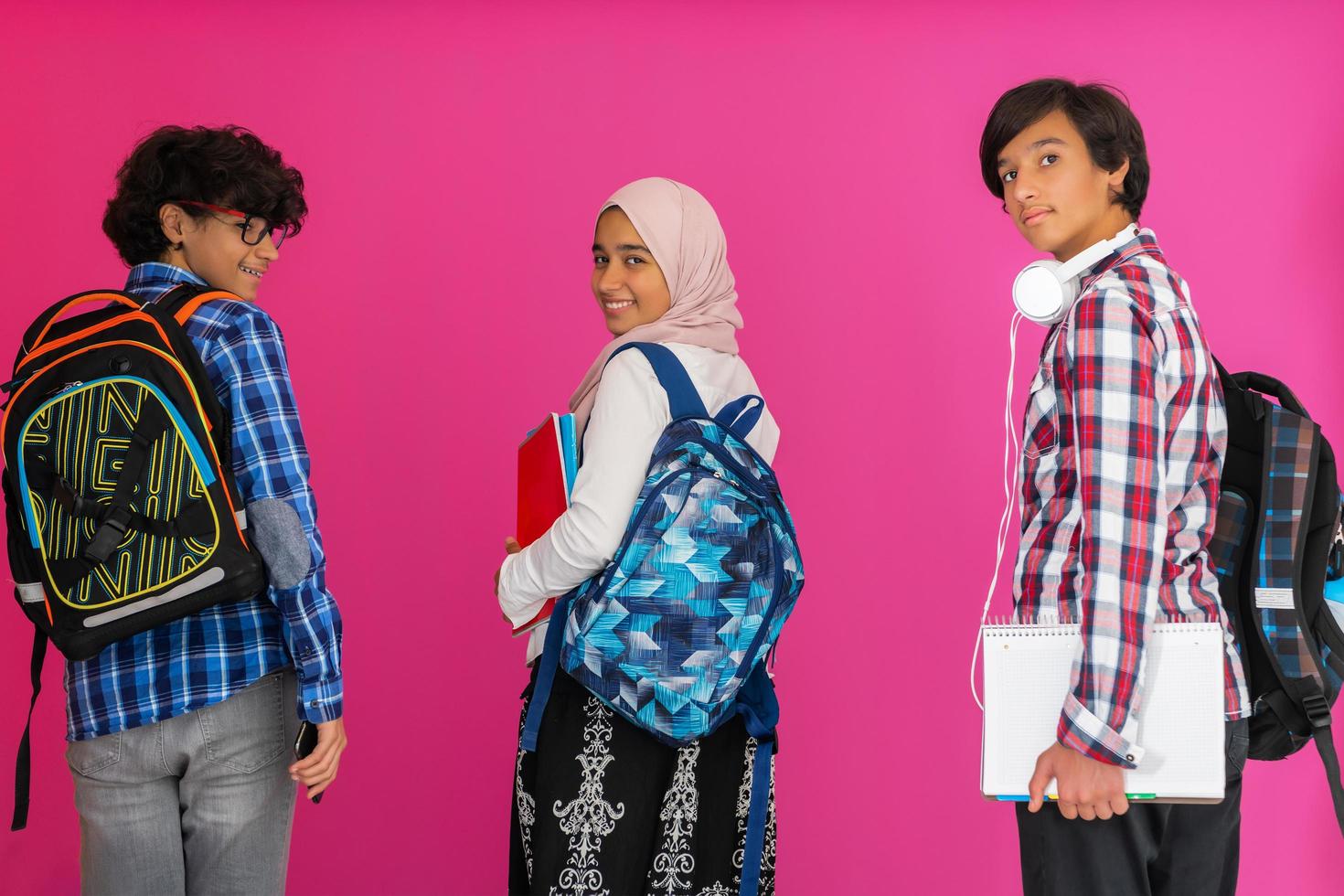 un' gruppo di arabo adolescenti, un' alunno squadra a piedi inoltrare in il futuro e indietro per scuola il concetto di un' rosa sfondo. il concetto di riuscito formazione scolastica per giovane le persone. selettivo messa a fuoco foto