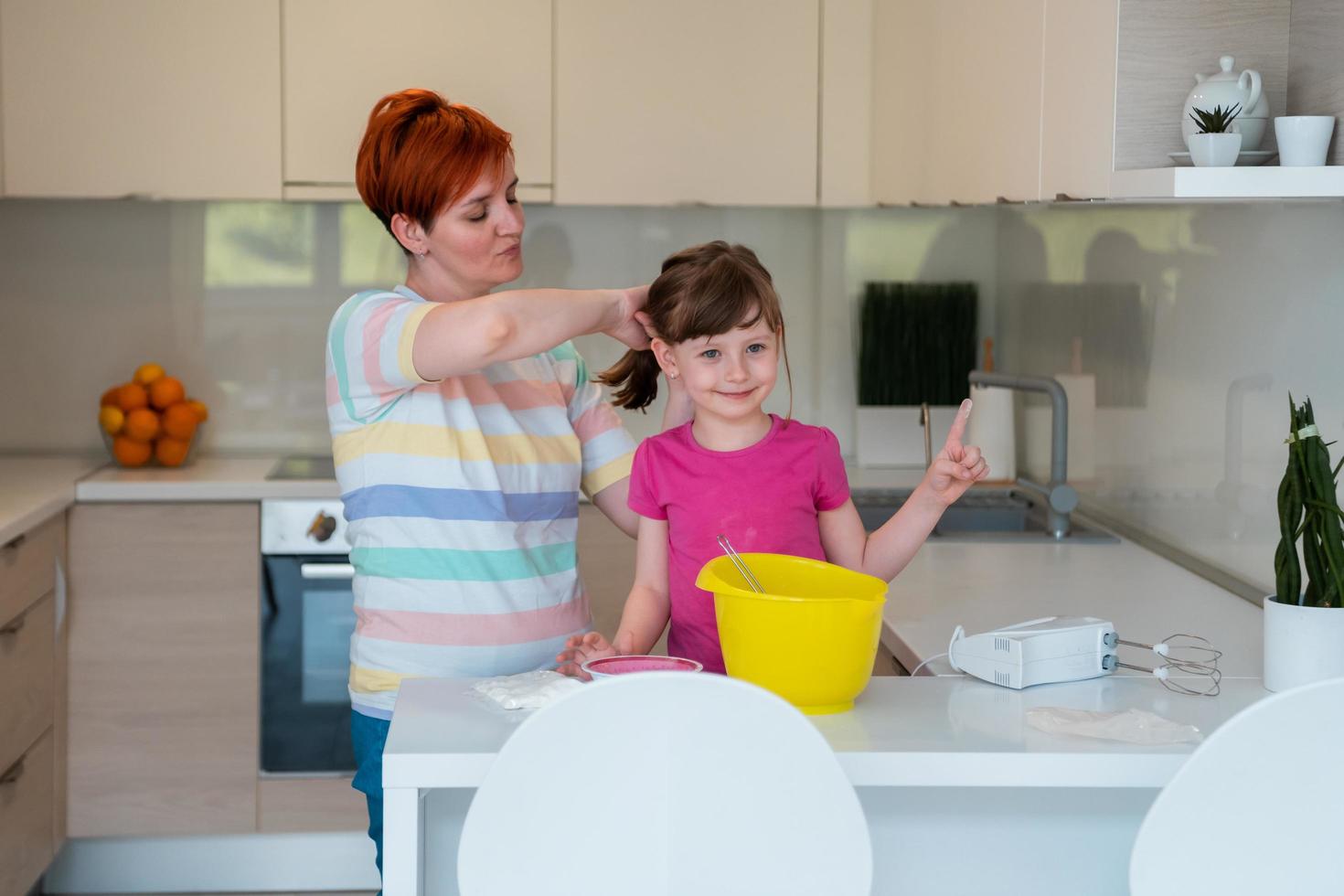 divertente poco ragazza aiutante giocando con Impasto su il suo mani apprendimento per impastare aiuta adulto mamma nel il cucina, contento carino bambino figlia e genitore mamma avere divertimento cucinando biscotti. foto