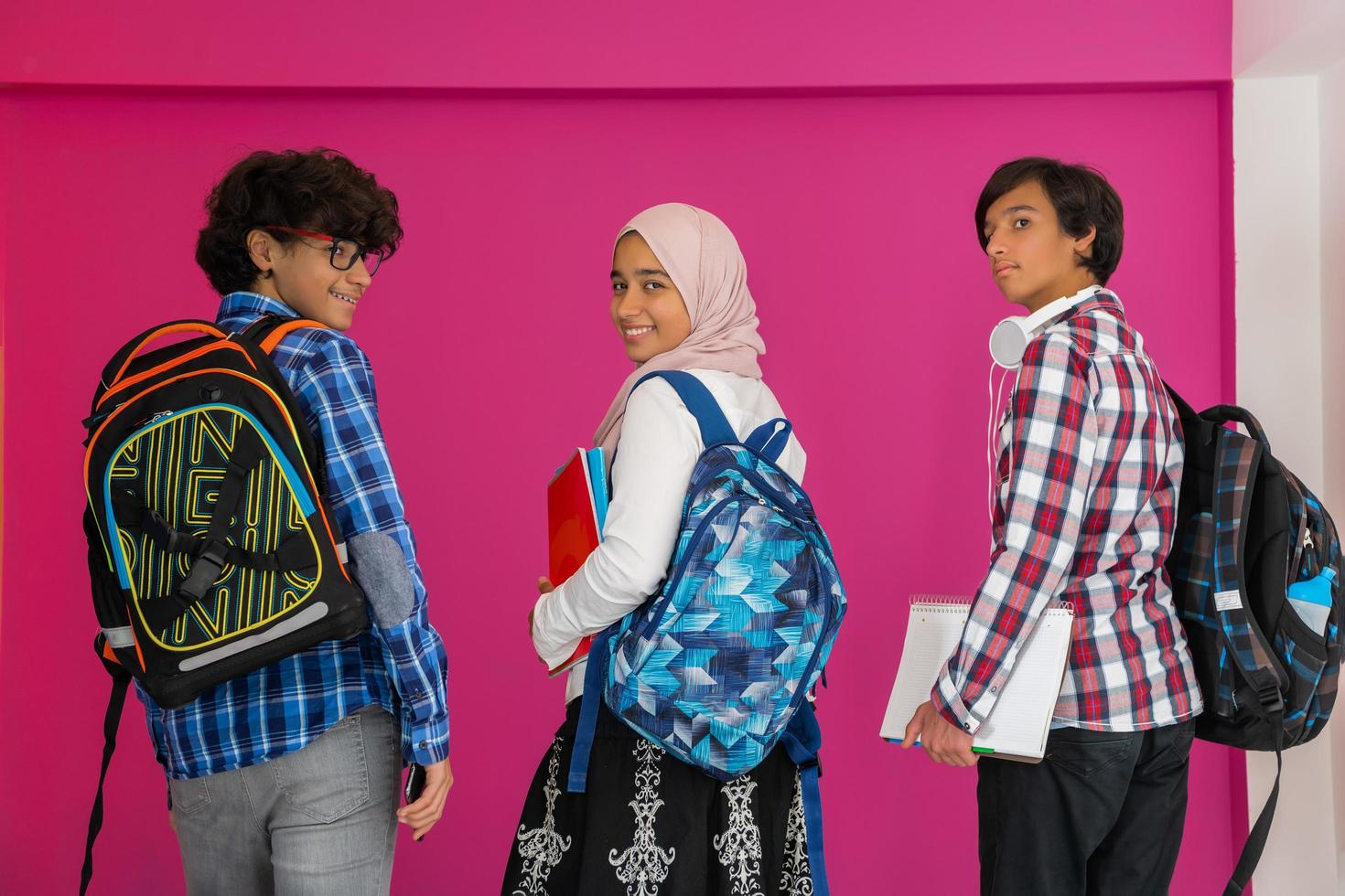 un' gruppo di arabo adolescenti, un' alunno squadra a piedi inoltrare in il futuro e indietro per scuola il concetto di un' rosa sfondo. il concetto di riuscito formazione scolastica per giovane le persone. selettivo messa a fuoco foto