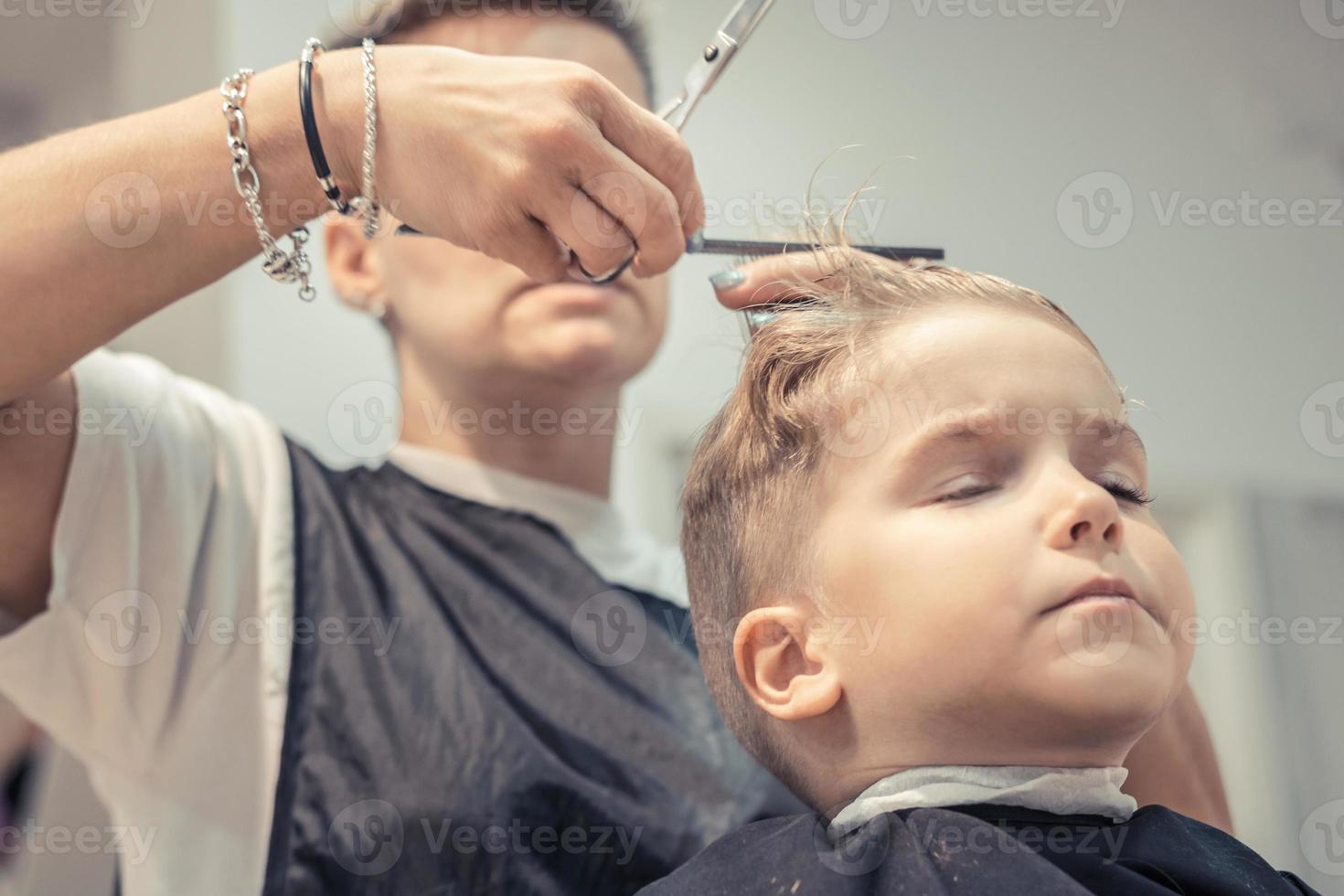 piccolo ragazzo durante taglio di capelli a capelli salone. foto