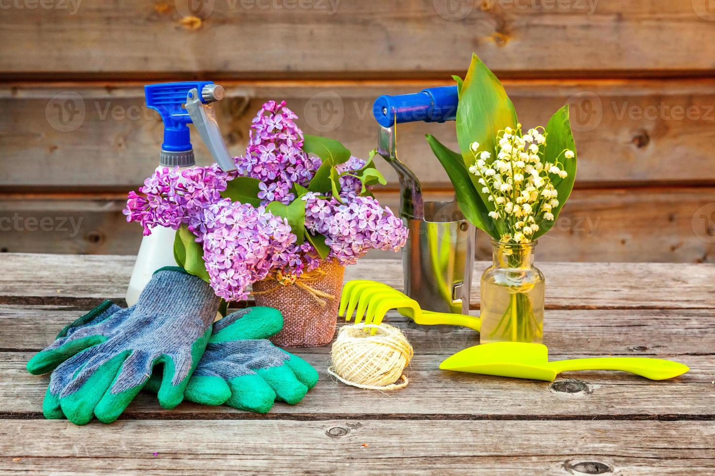 giardinaggio Strumenti, irrigazione Potere, pala, vanga, potatore, rastrello, guanto, lilla, giglio di il valle fiori su Vintage ▾ di legno tavolo. primavera o estate nel giardino, eco, natura, orticoltura passatempo concetto. foto