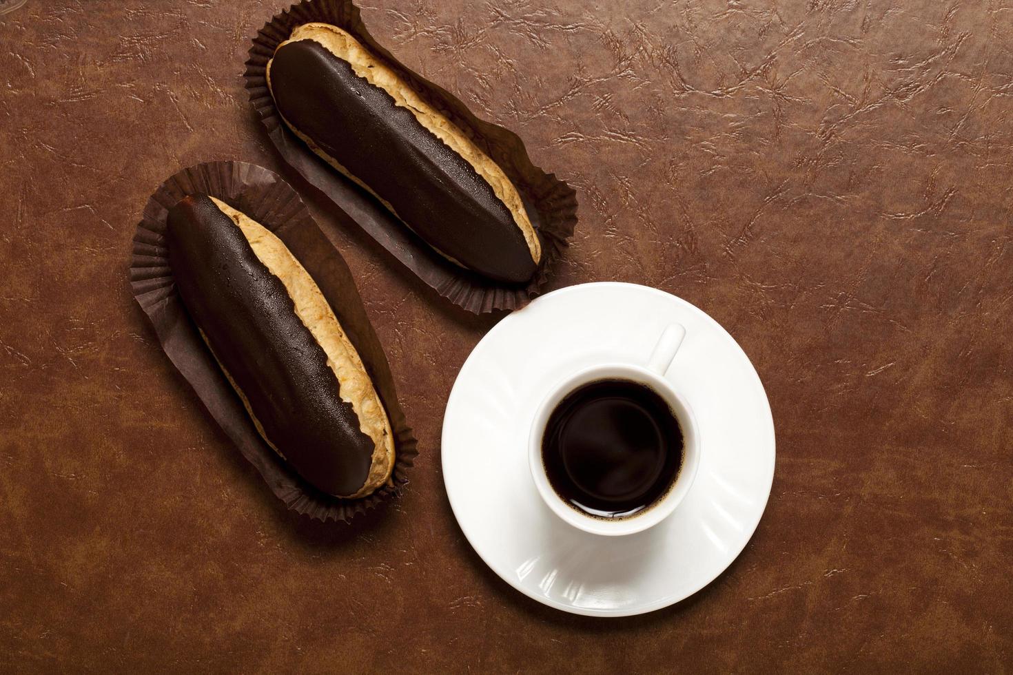 caffè, cioccolato eclair, caffè nel un' bianca tazza, bianca piattino, su un' Marrone tavolo, pasticcino su carta In piedi foto