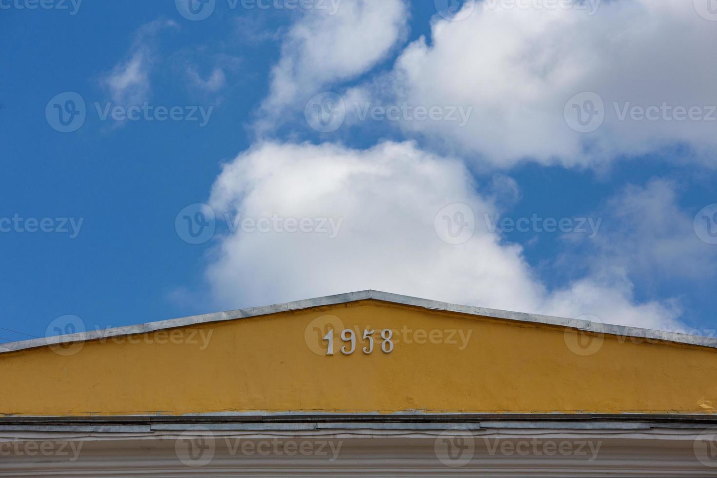 avvicinamento Visualizza di giallo tetto cresta spirito cifre 1958 su blu cielo con bianca nuvole sfondo foto