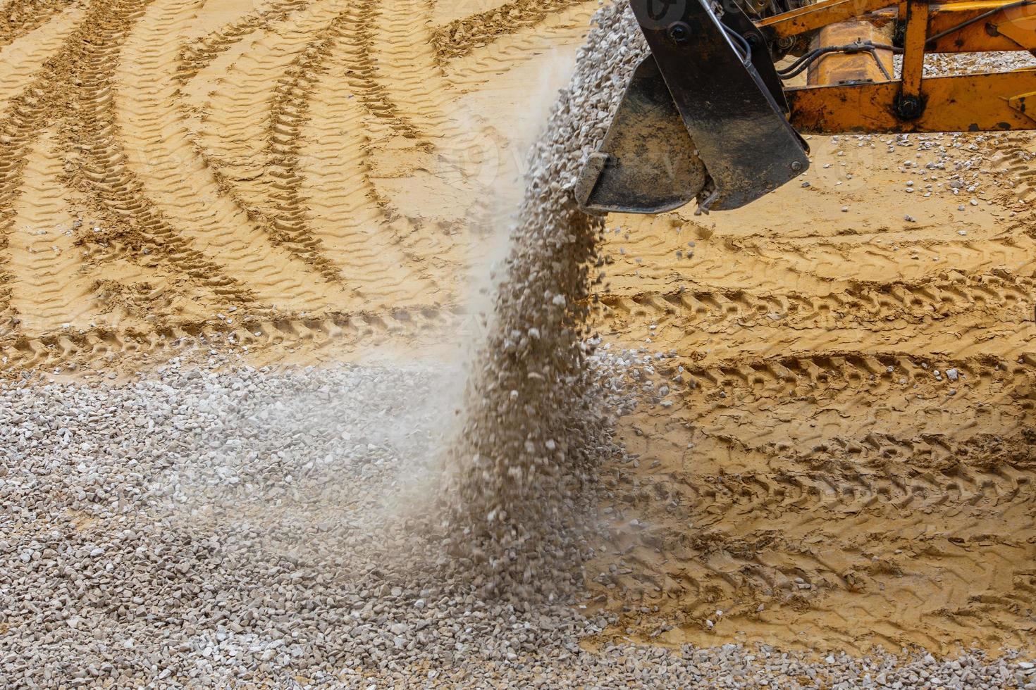 un' bulldozer versa ghiaia a partire dal un' secchio su il compatto sabbia a un' costruzione luogo foto