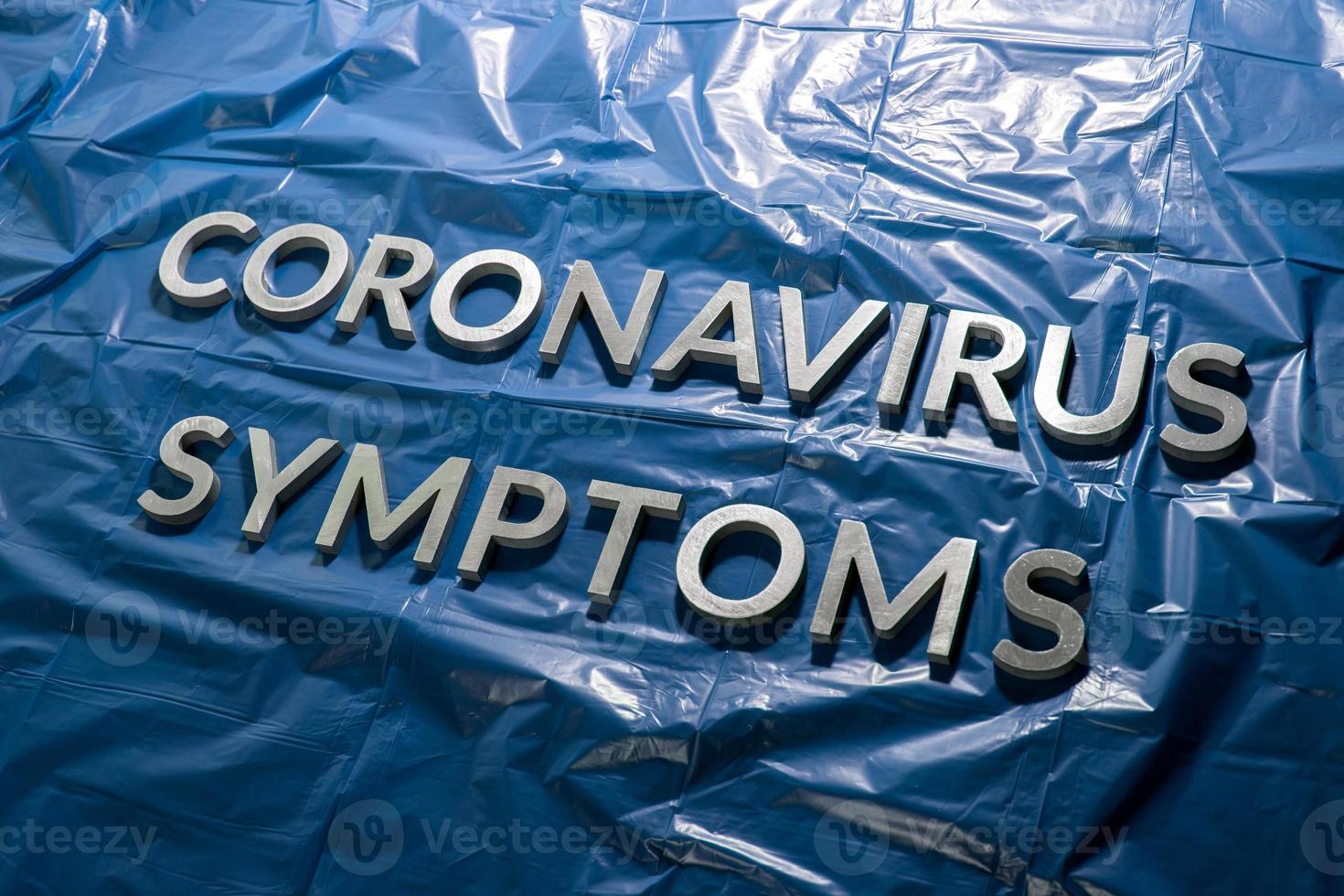 il parole coronavirus sintomi di cui con argento lettere su spiegazzato blu plastica film - diagonale prospettiva composizione foto
