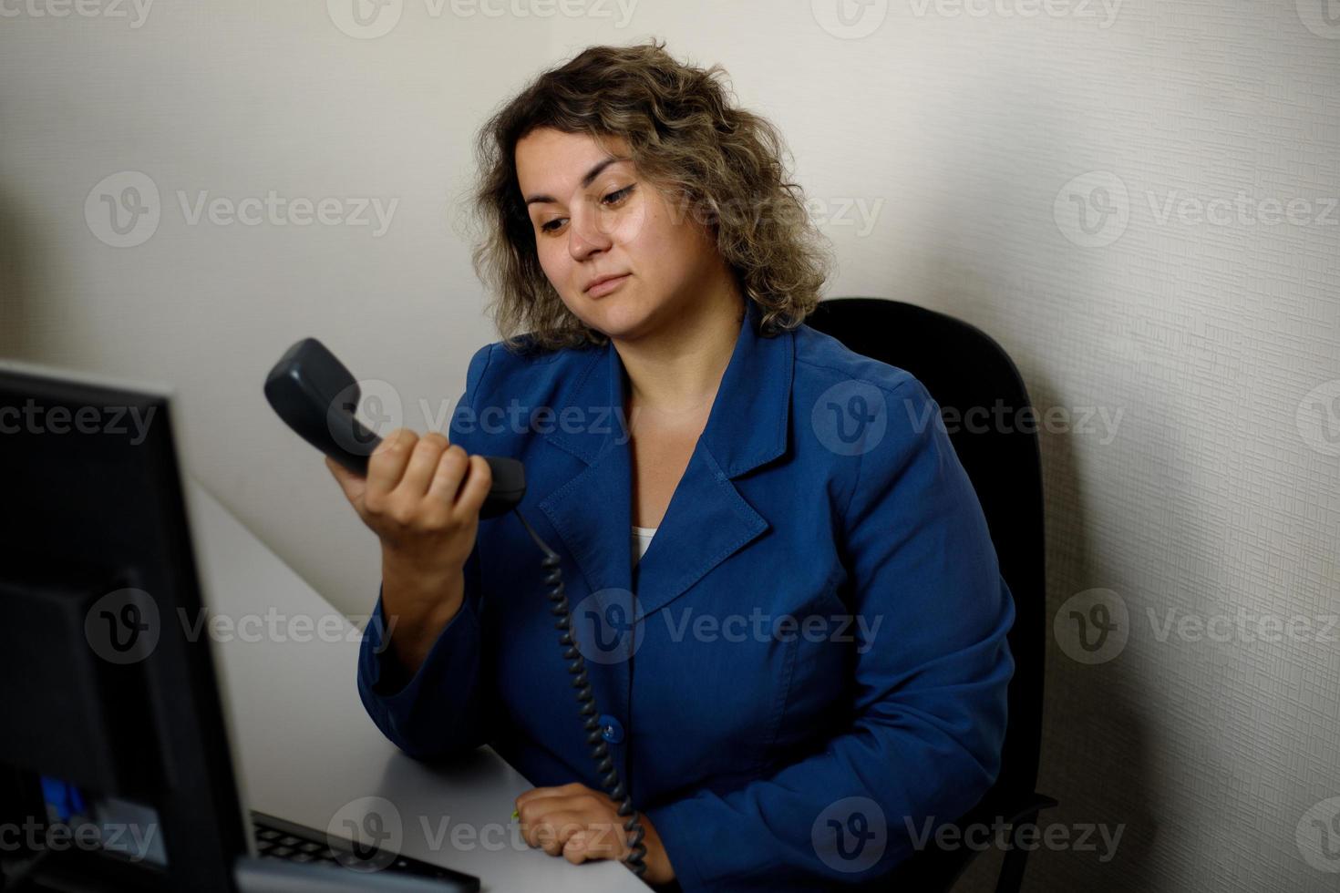 un' giovane donna si siede a un ufficio scrivania nel perplessità, non posso ottenere attraverso su il Telefono. televenditore, telemarketing agente, ufficio dipendente. foto