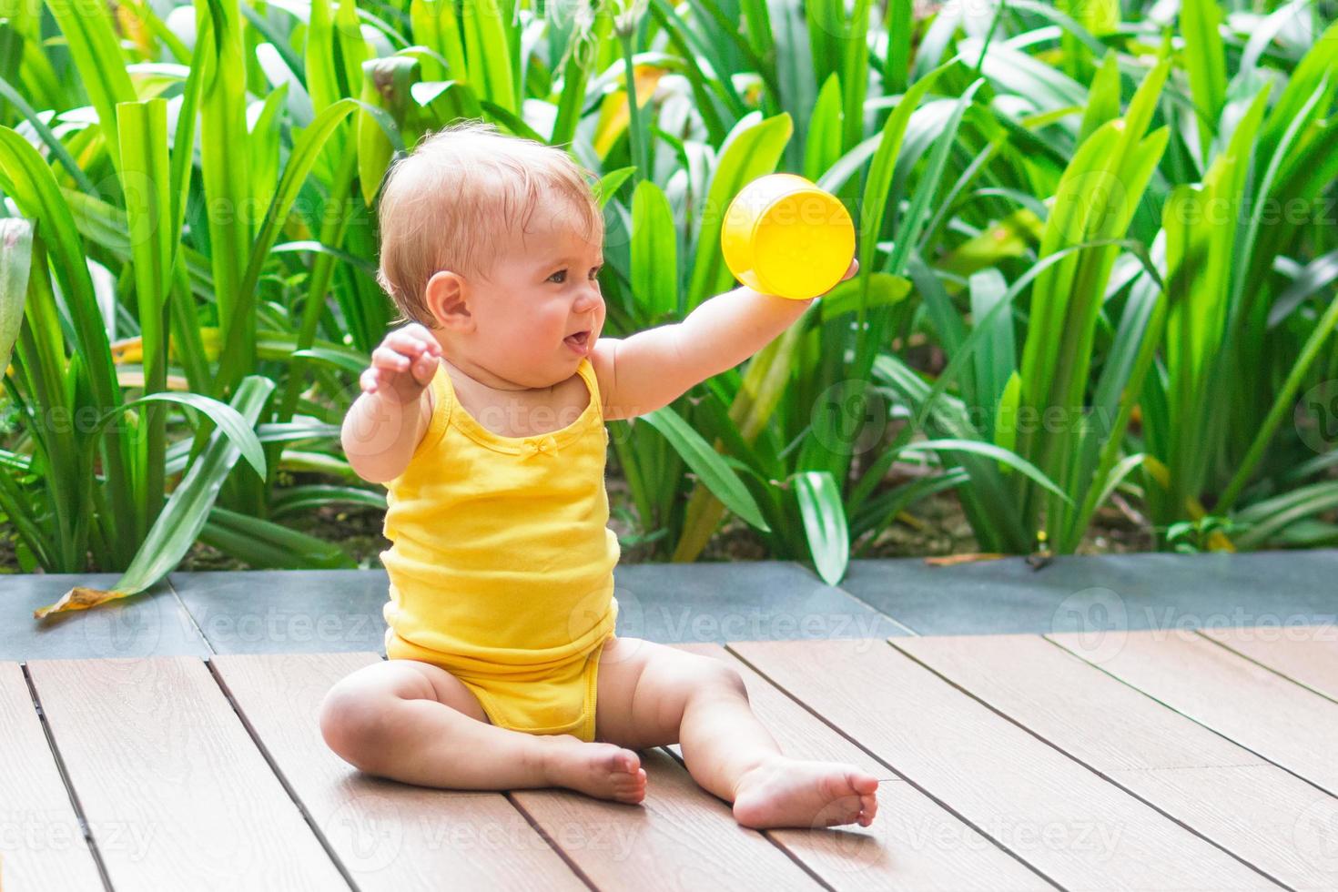 poco ragazza giocando all'aperto con colorato plastica costruttore su un' sfondo di verde impianti. foto