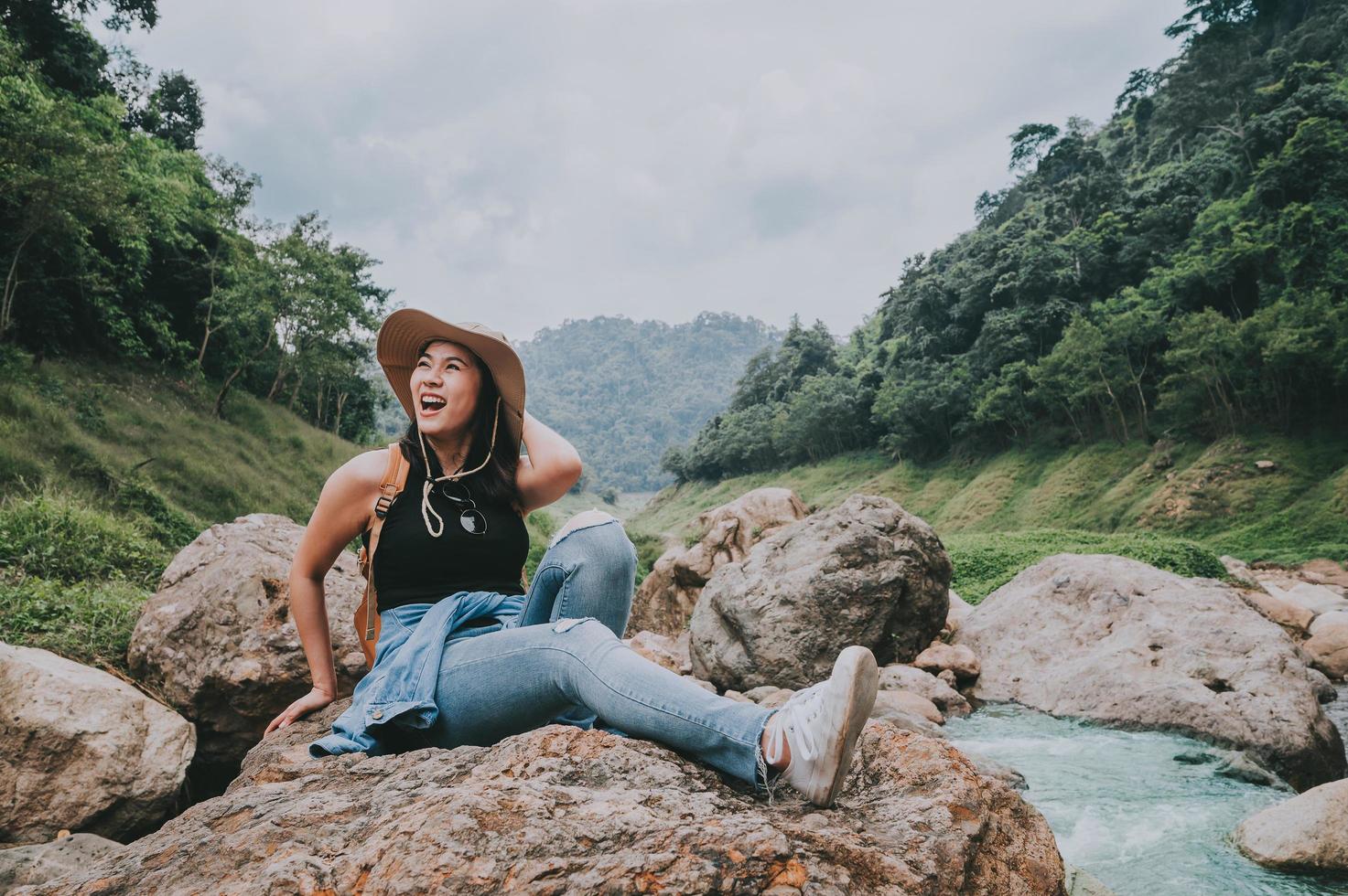 donna felice che ride mentre era seduto sulla roccia dal fiume foto