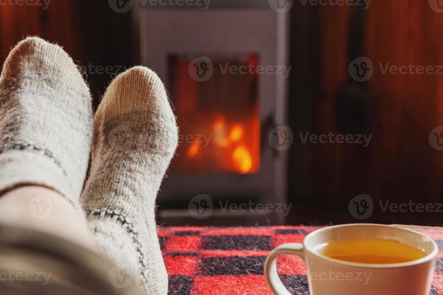 piedi gambe nel inverno Abiti lana calzini e tazza tè a camino sfondo. donna seduta a casa su inverno o autunno sera rilassante e riscaldamento su. inverno e freddo tempo atmosferico. hygge Natale vigilia foto