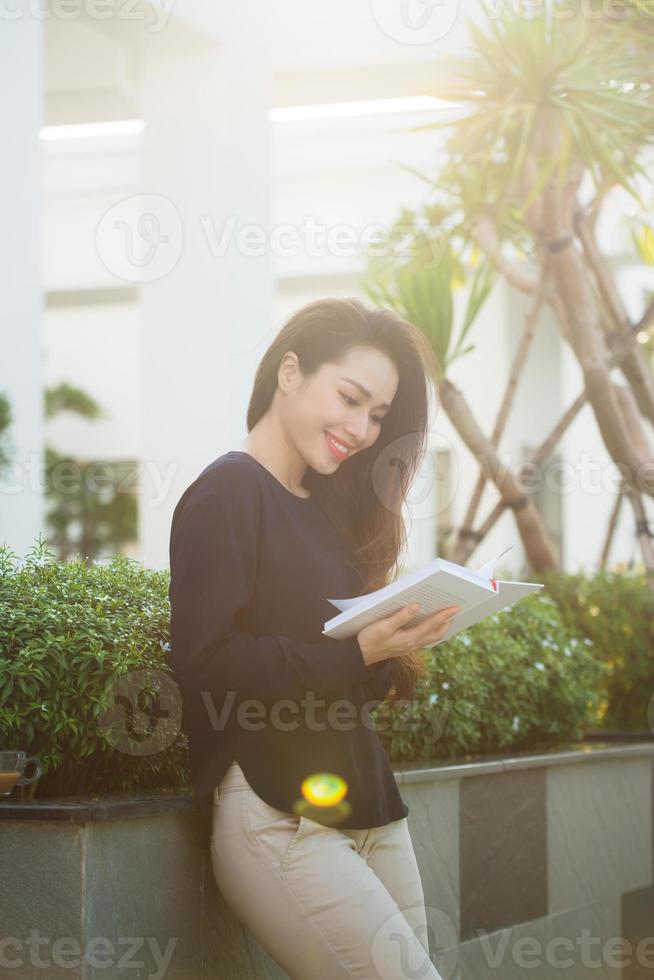 contento giovane donna Tenere libro affettuoso di letteratura analizzando romanzo durante tempo libero tempo su terrazza di città universitaria bar nel soleggiato giorno. foto