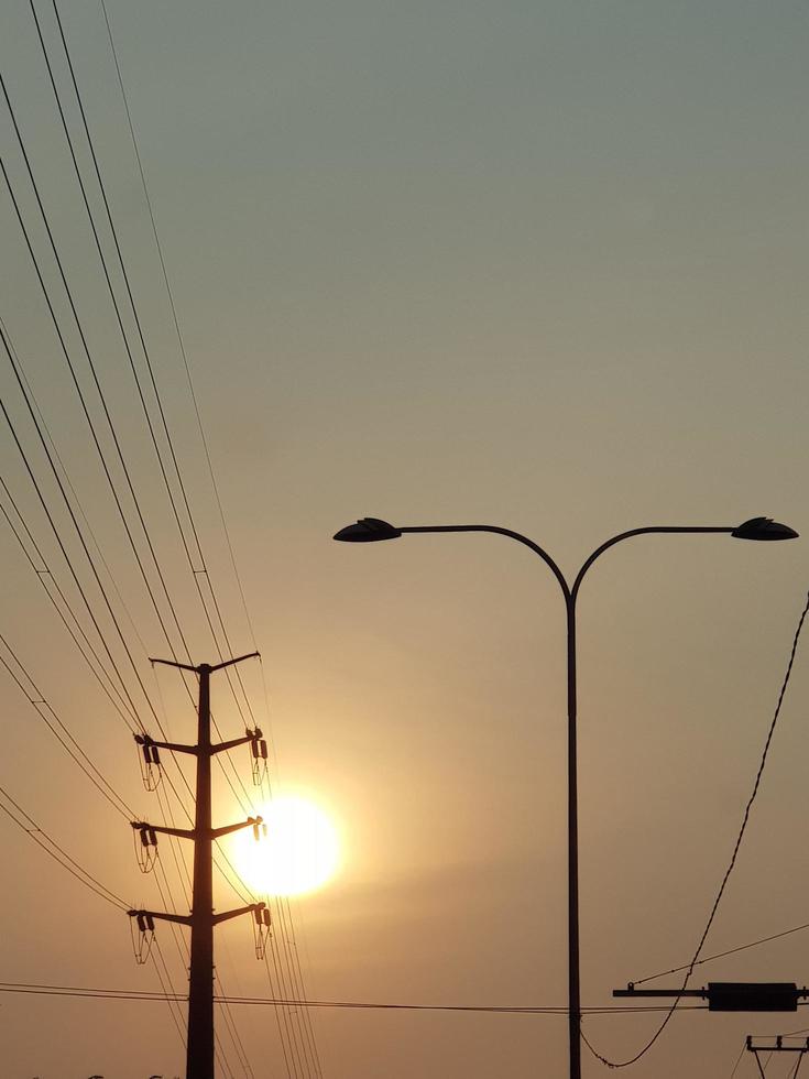 il sole a crepuscolo con sagome di elettrico poli e lampada messaggi. foto